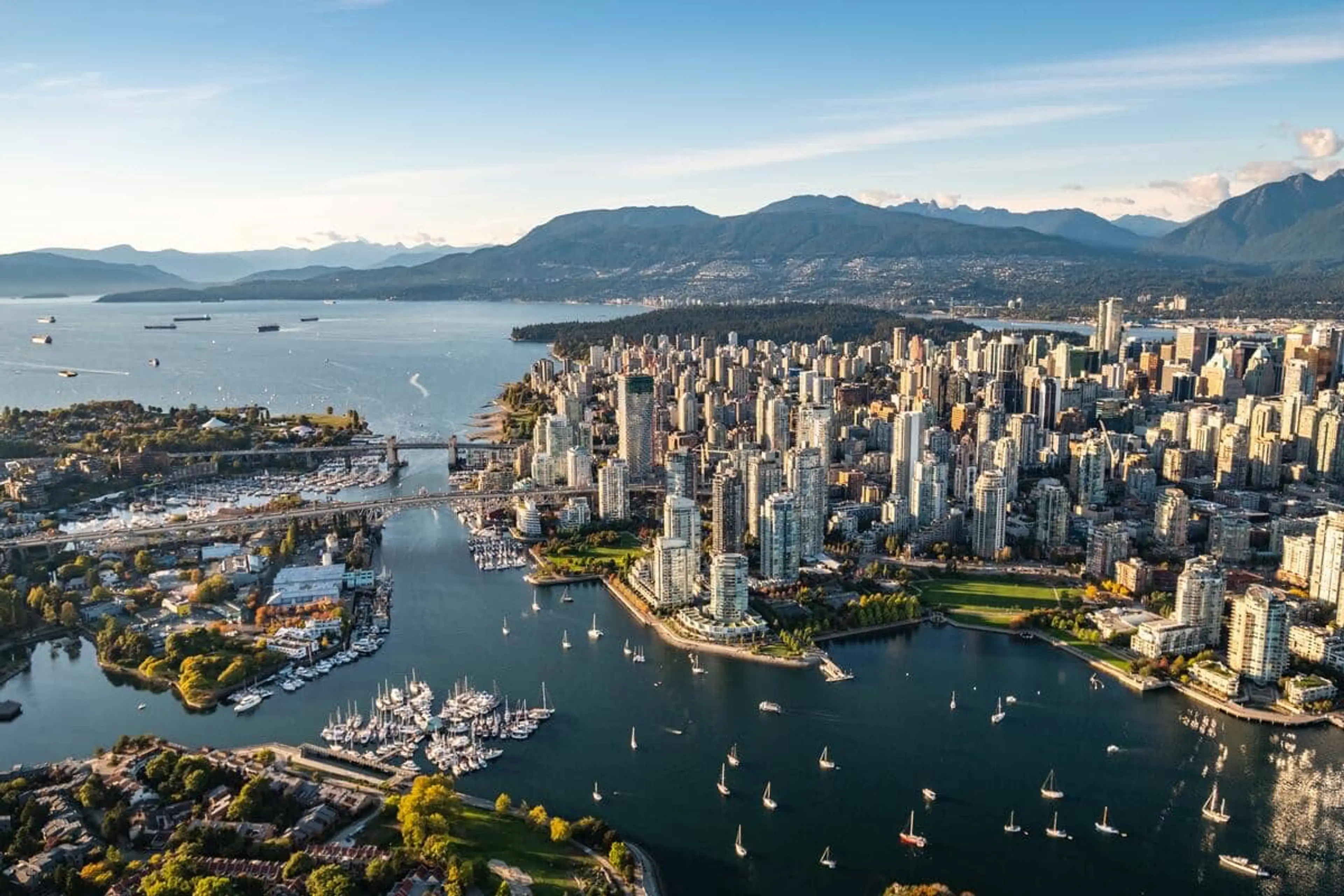 Aerial view of downtown Vancouver with False Creek, sailboats, and coastal mountains in the background.