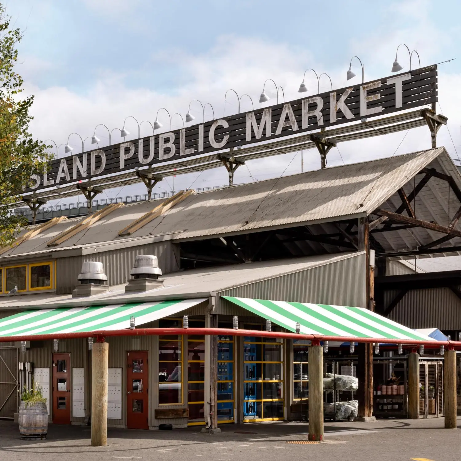 Exterior of a public market building with a large sign reading 'ISLAND PUBLIC MARKET' and green and white striped awnings.