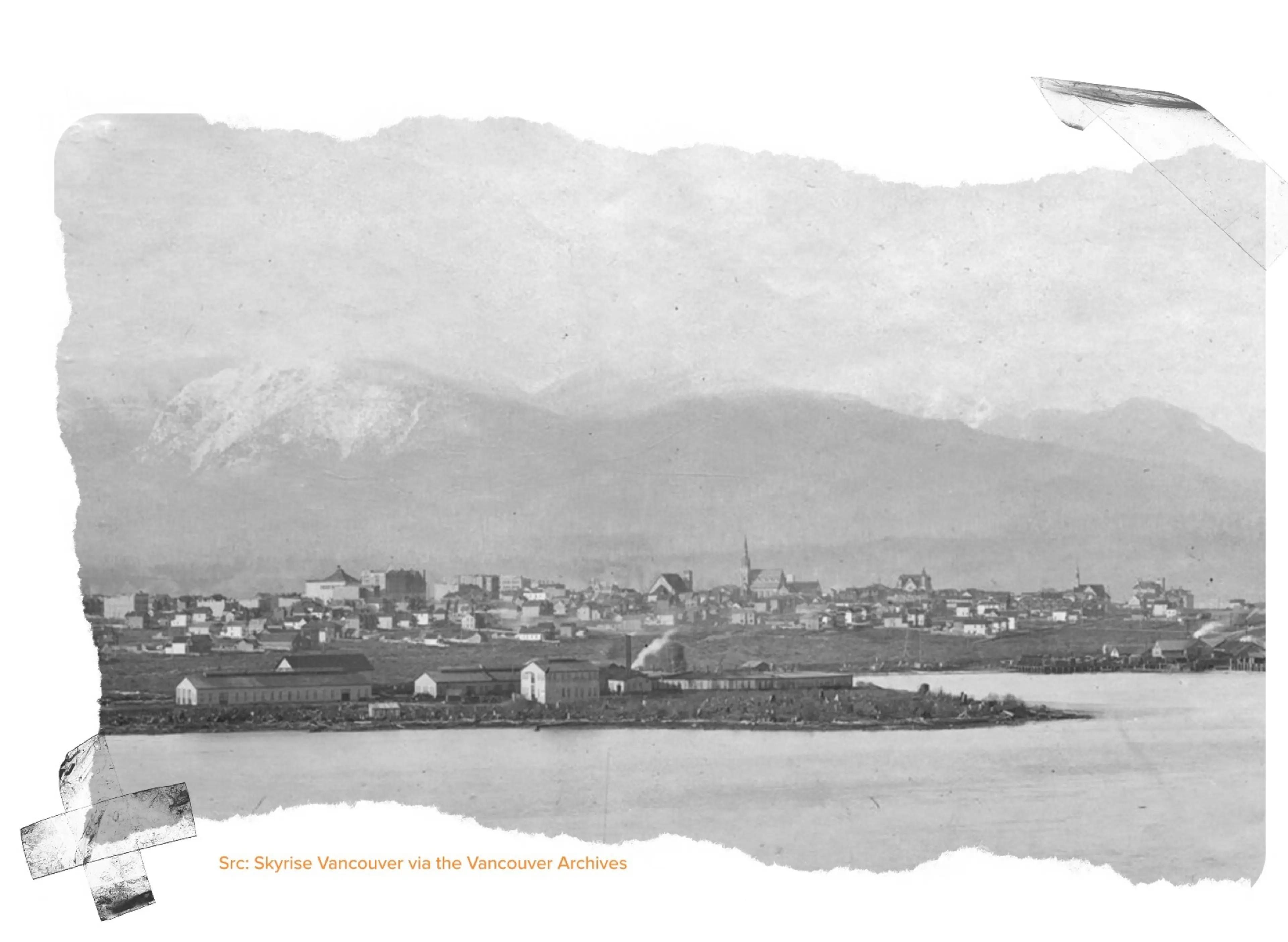 Black and white panoramic view of a town with buildings near a body of water and mountains in the background.