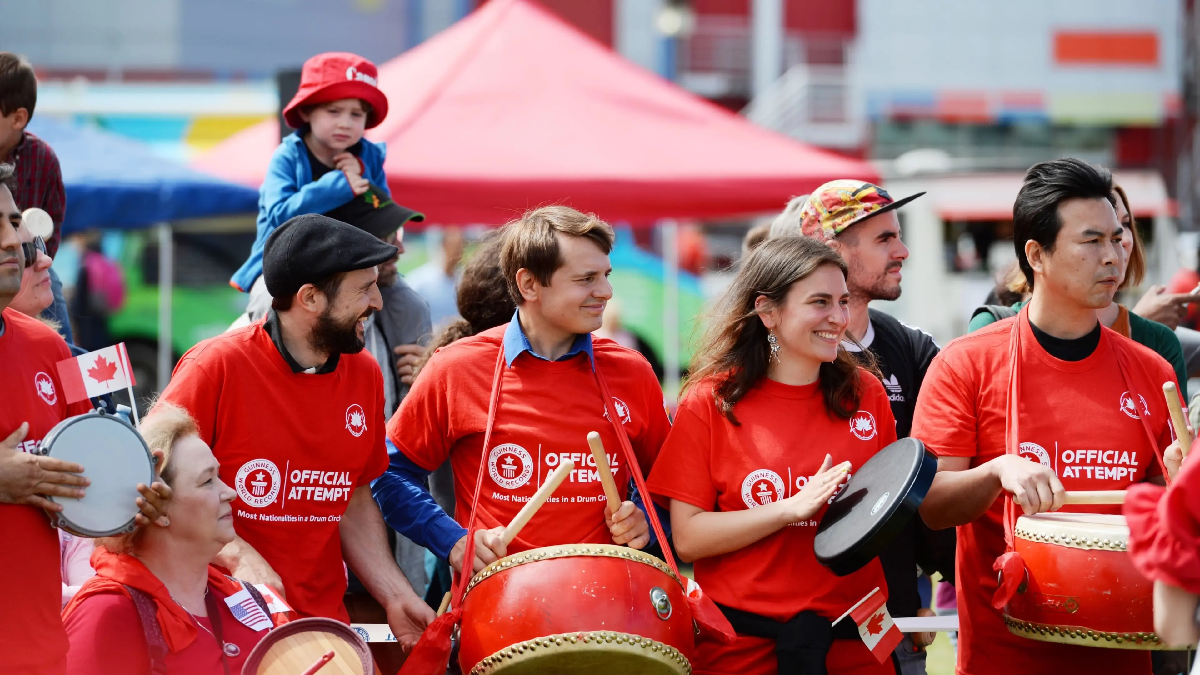 A group of people wearing red shirts with 'Official Attempt' text, playing drums and tambourines at an outdoor event.