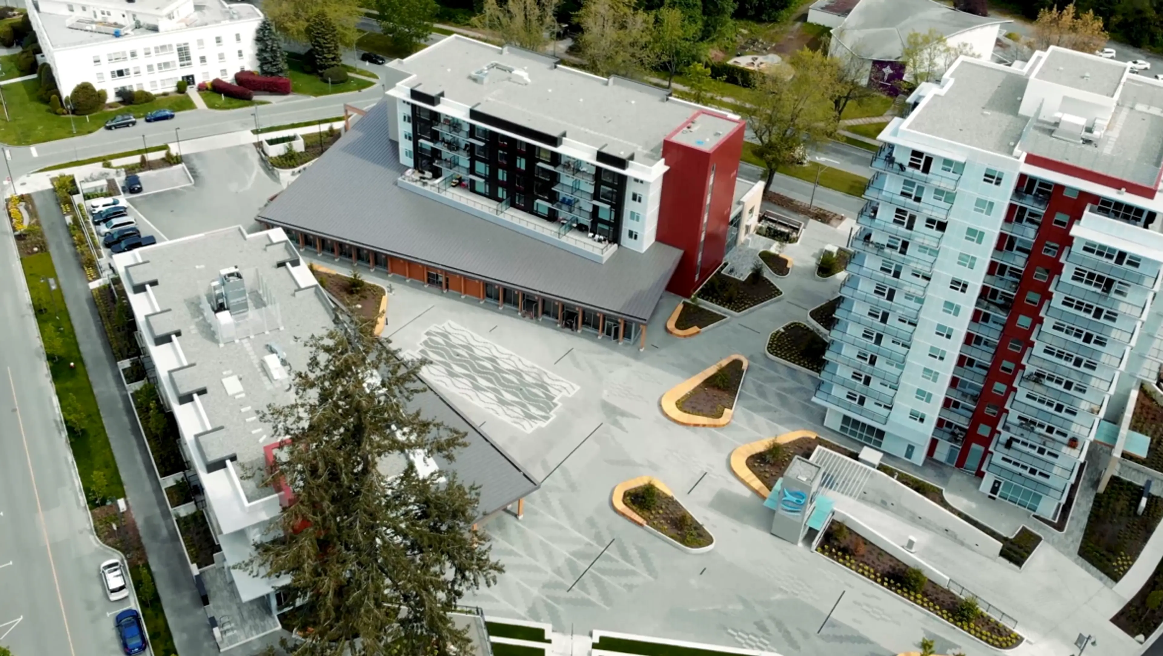 Aerial view of modern multi-story buildings surrounding a large open courtyard with geometric landscaping and pathways.