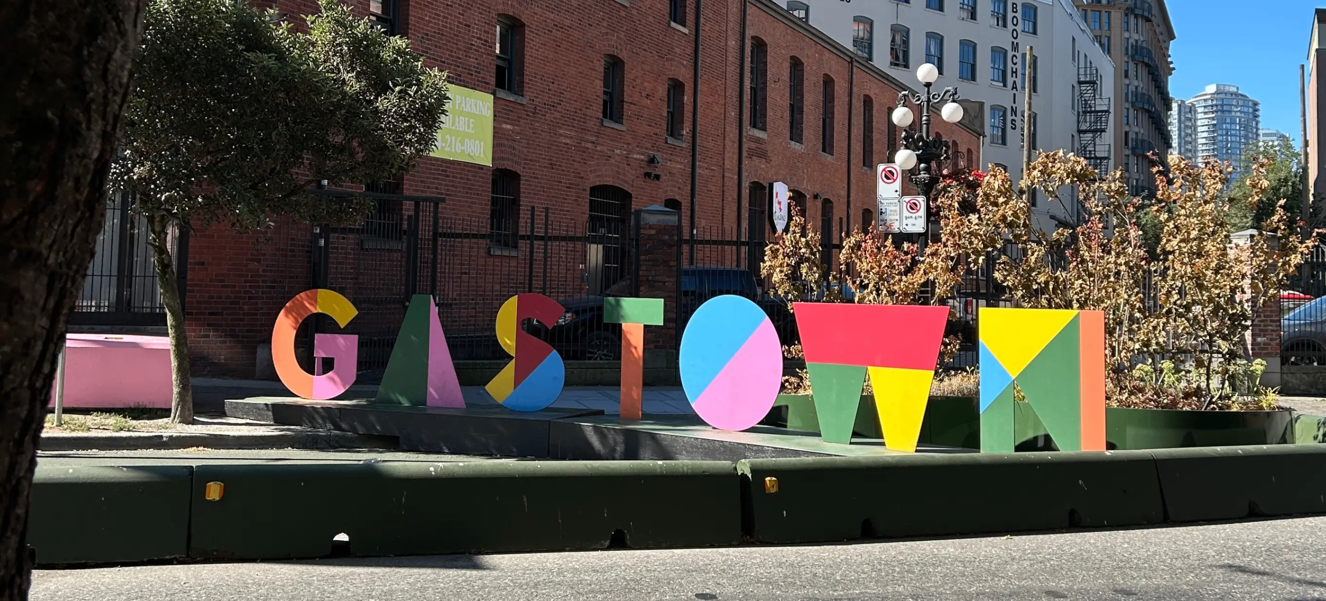 Colorful block letters spelling GASTOWN on a street curb with brick buildings and trees in the background.