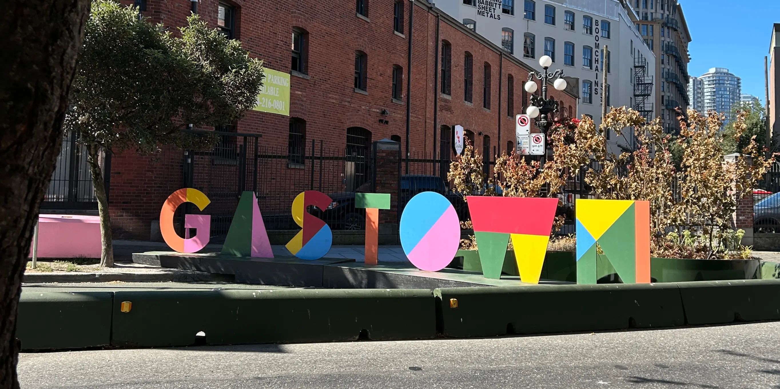 Colorful block letters spelling GASTOWN on a street curb with brick buildings and trees in the background.