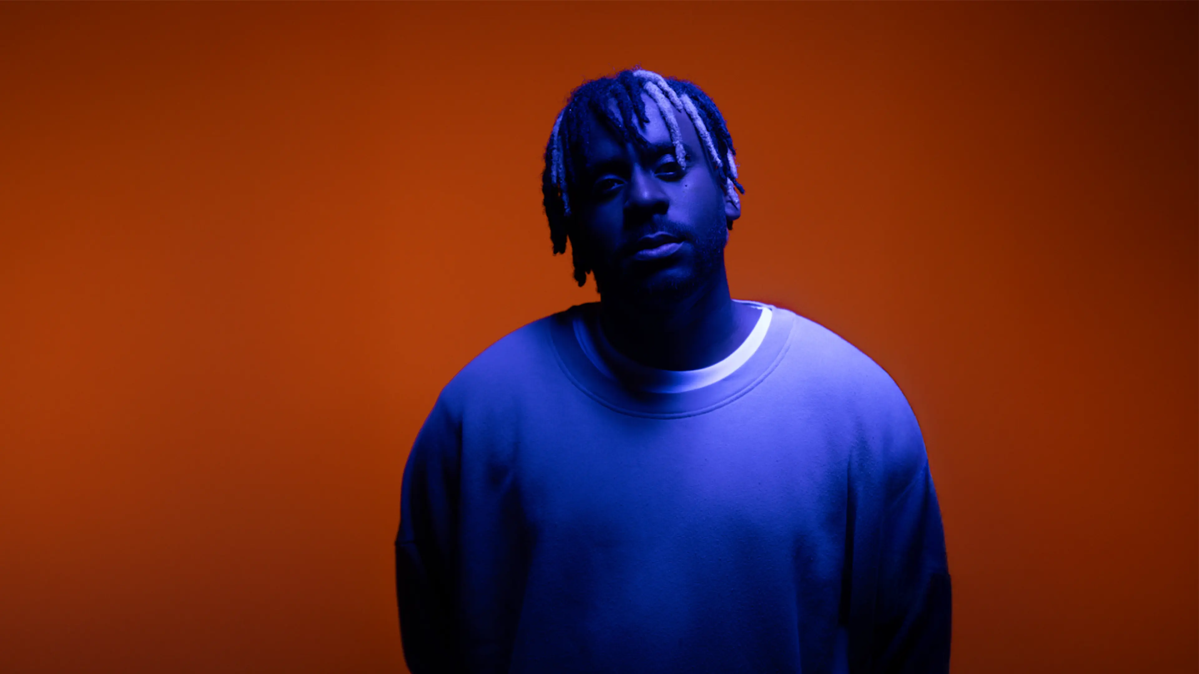 Person with blue lighting wearing a sweatshirt against an orange background.