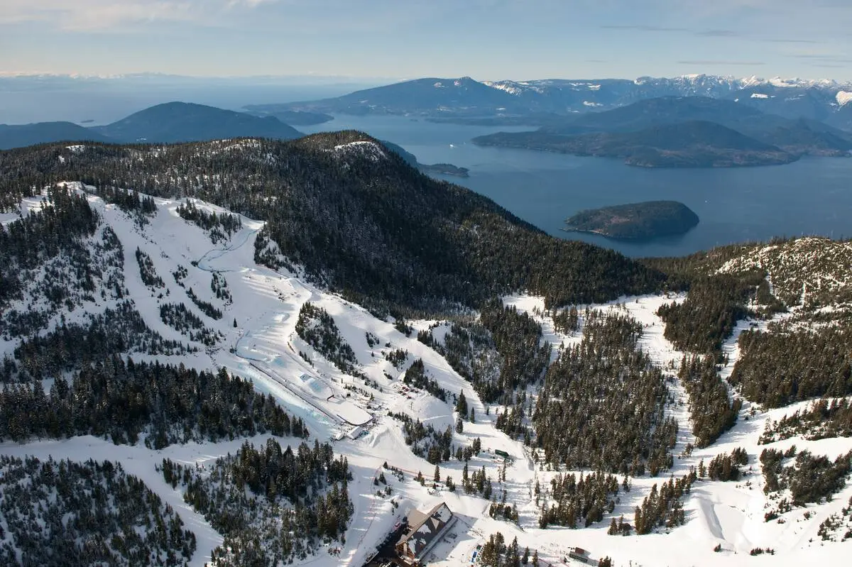 Aerial view of snowy ski runs at Cypress Mountain with the ocean in the background.