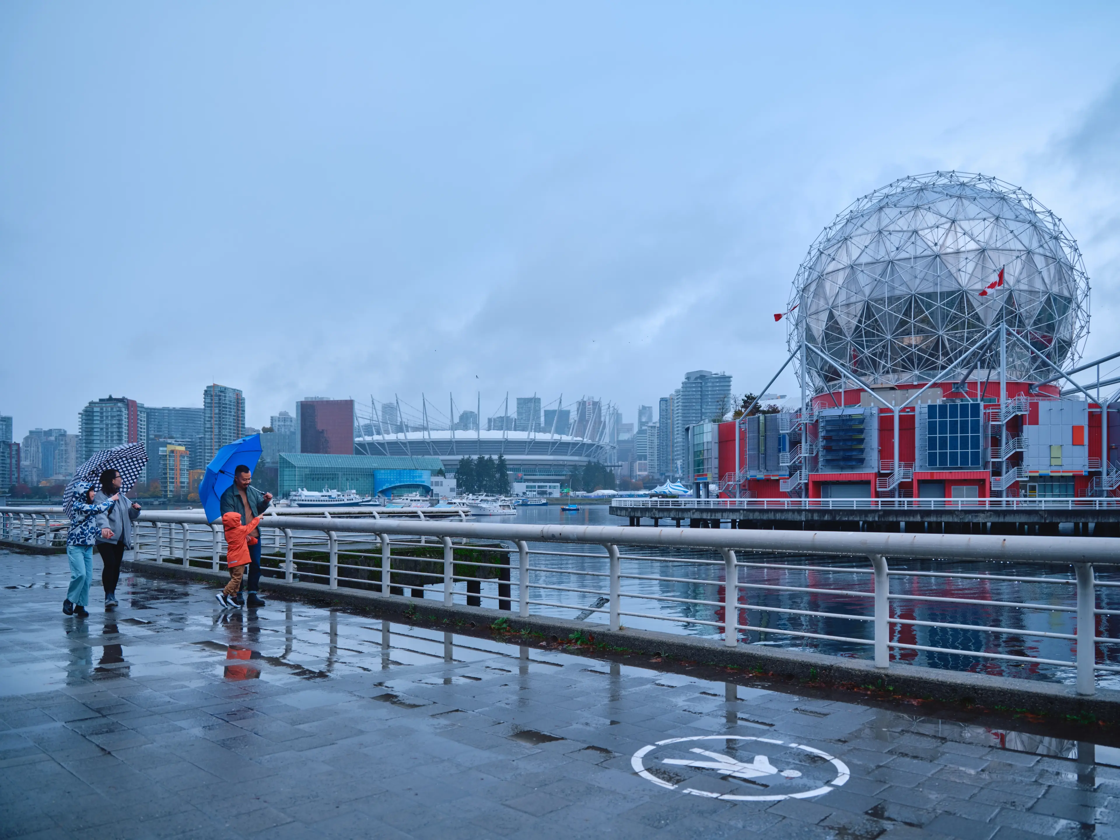 A family waking in the rain with views of Science World in Vancouver.