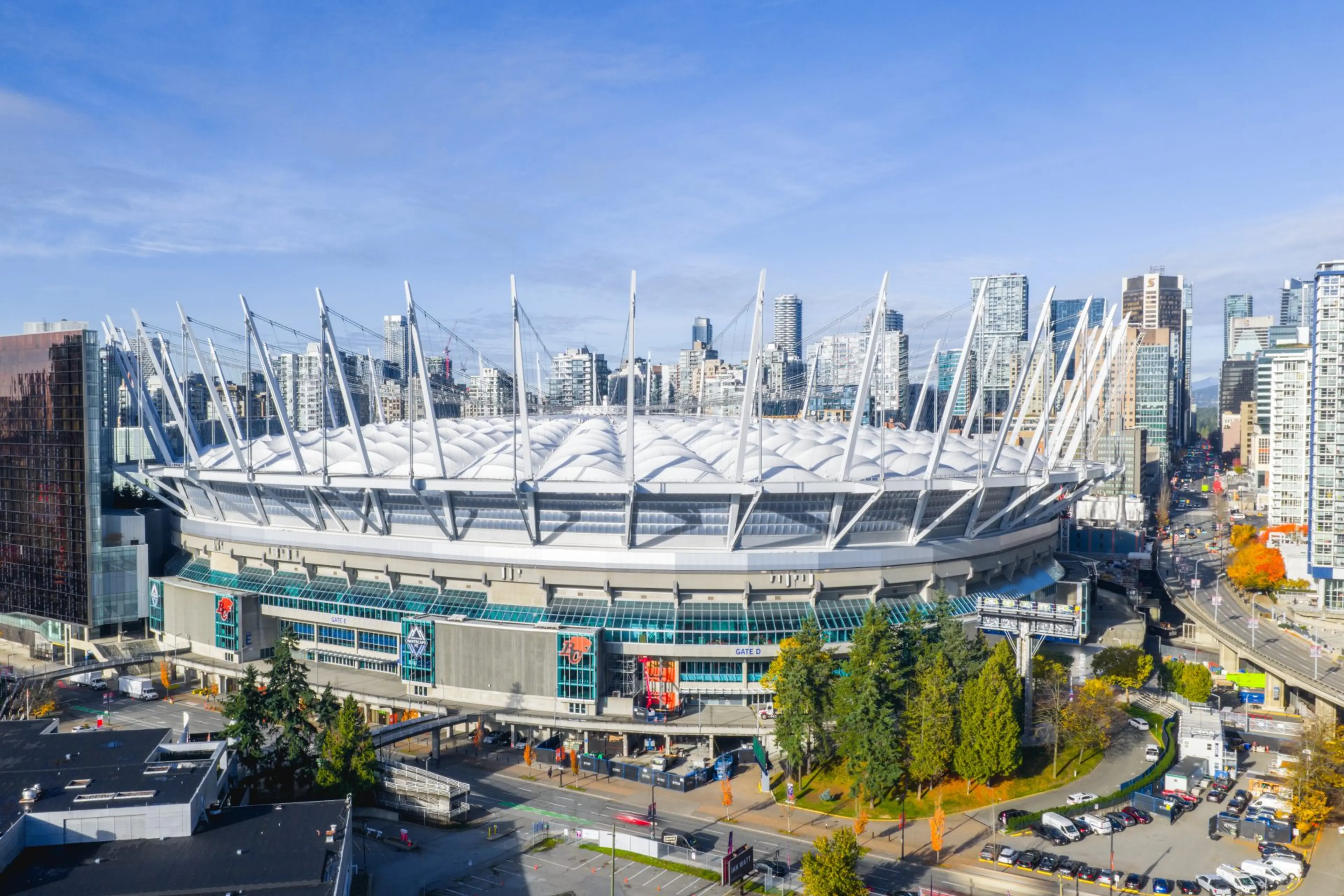BC Place stadium surrounded by city buildings and trees under a clear blue sky.