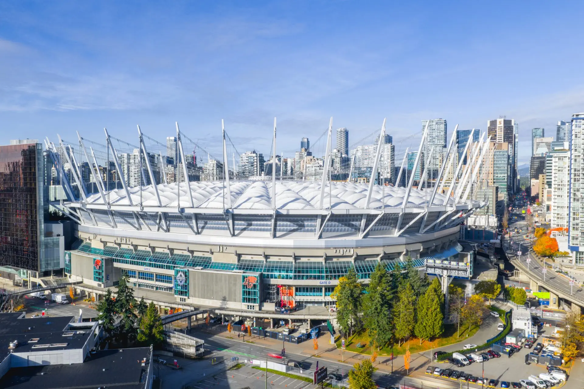 BC Place stadium surrounded by city buildings and trees under a clear blue sky.