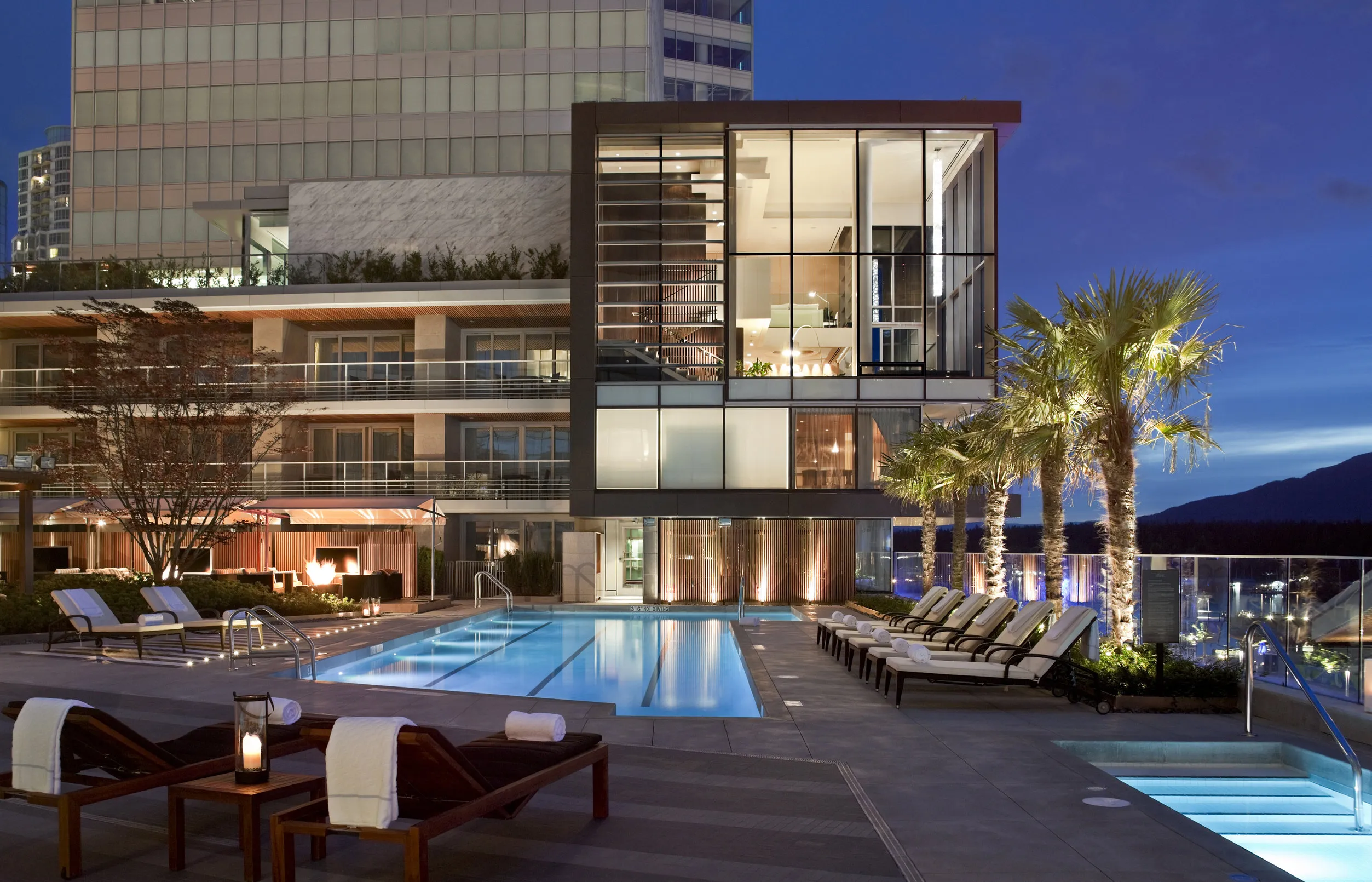 A modern luxury hotel with a pool and palm trees at night
