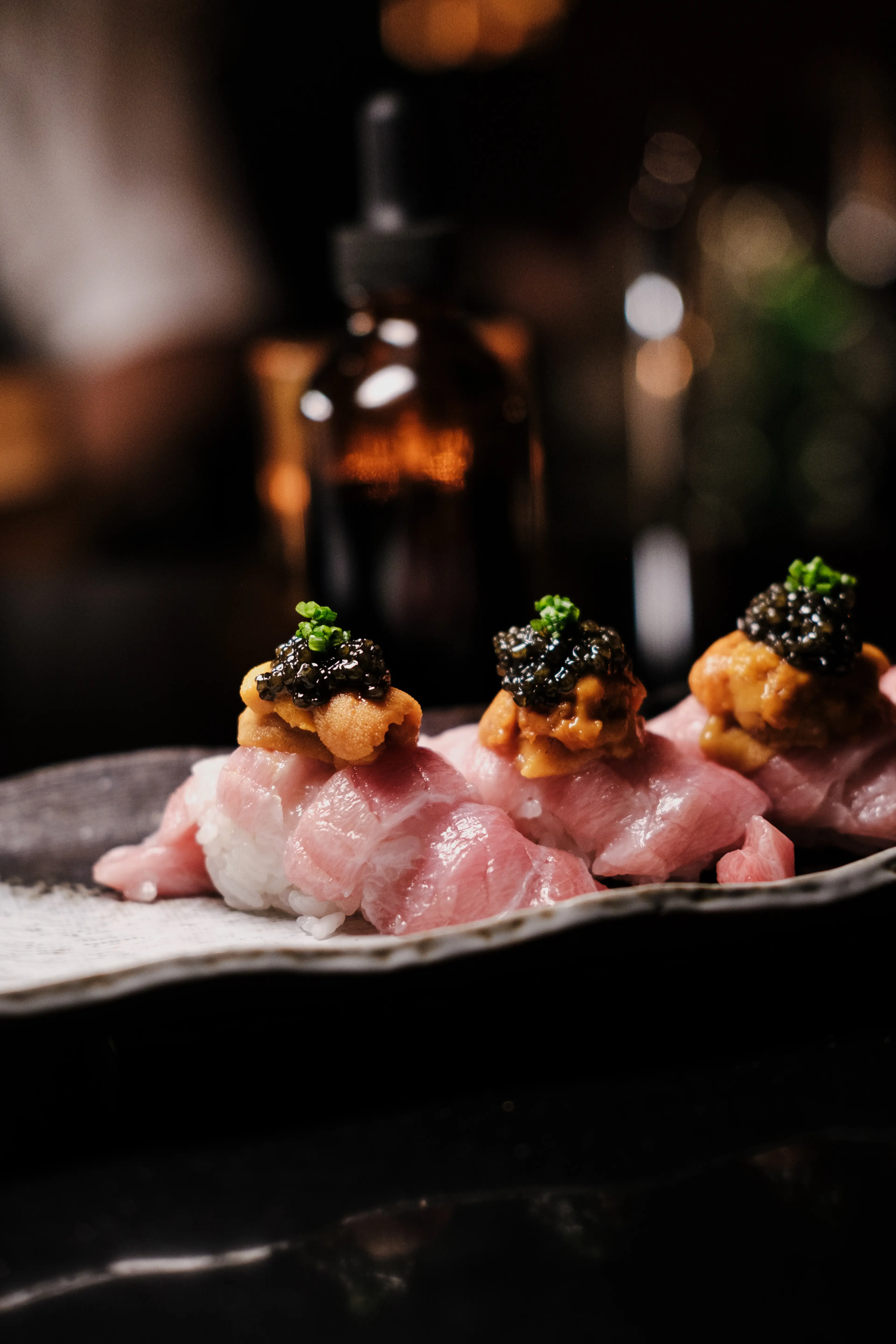 Three pieces of sushi topped with sea urchin, black caviar, and green garnish on a ceramic plate.