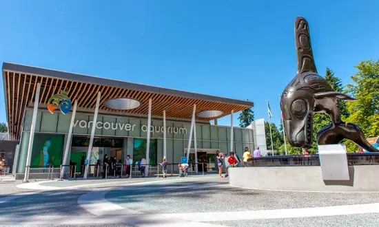 Exterior of Vancouver Aquarium with people outside and a large black whale sculpture on the right.