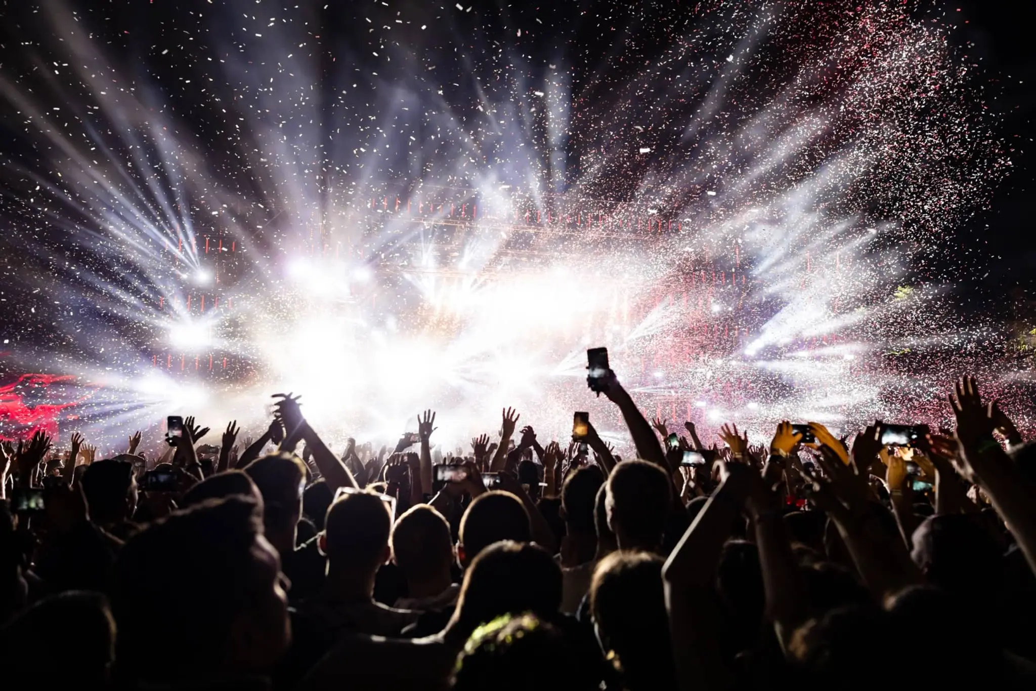 Crowd at a night concert with hands raised and bright stage lights with confetti in the air