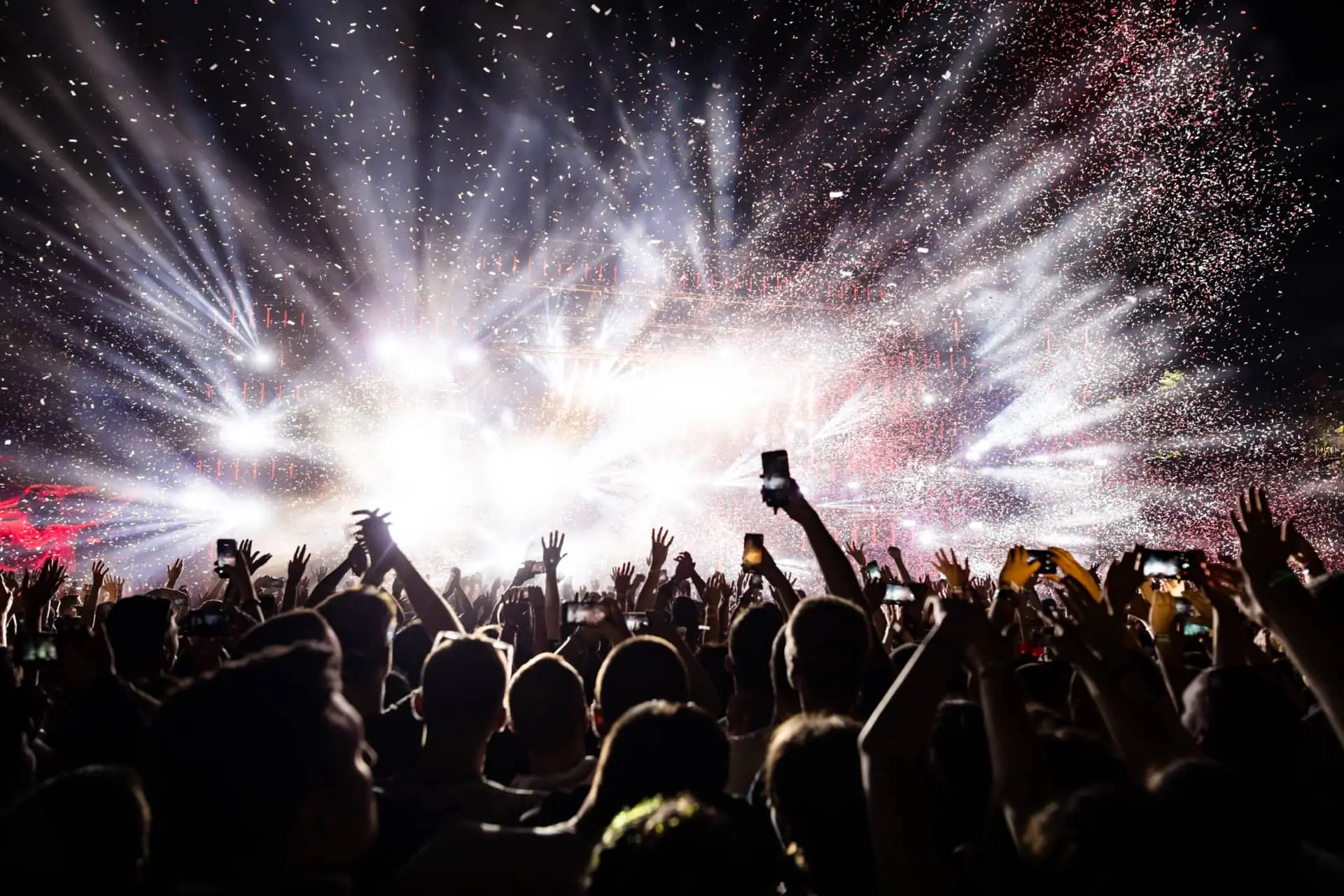 Crowd at a night concert with hands raised and bright stage lights with confetti in the air