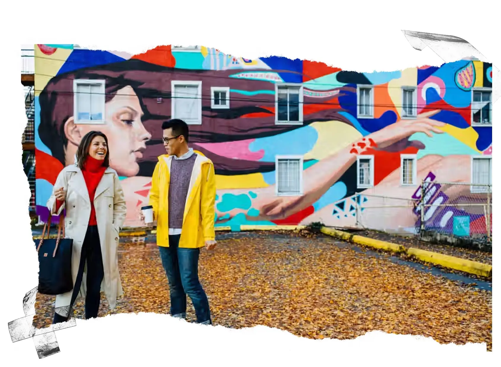 Two people standing and talking in front of a colorful mural of a woman with flowing hair on a building wall.