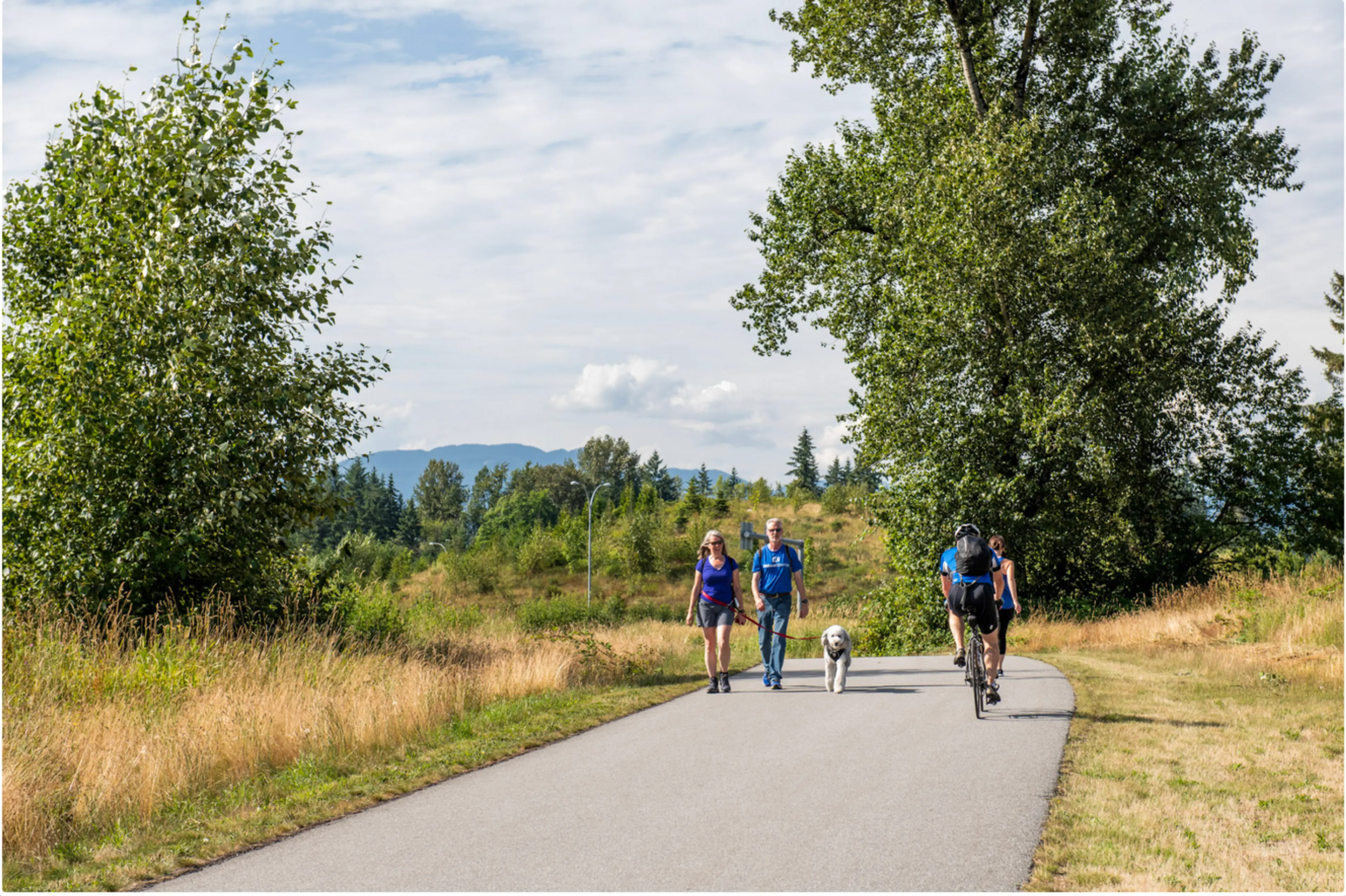 A cyclist and walkers on the paved Perimeter Trail in Tynehead Regional Park