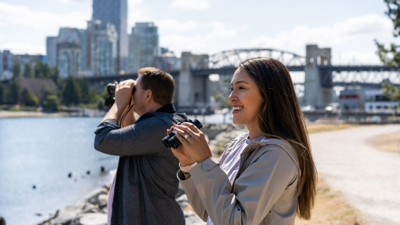 A man and a woman hold binoculars and look for birds in Vanier Park in Vancouver