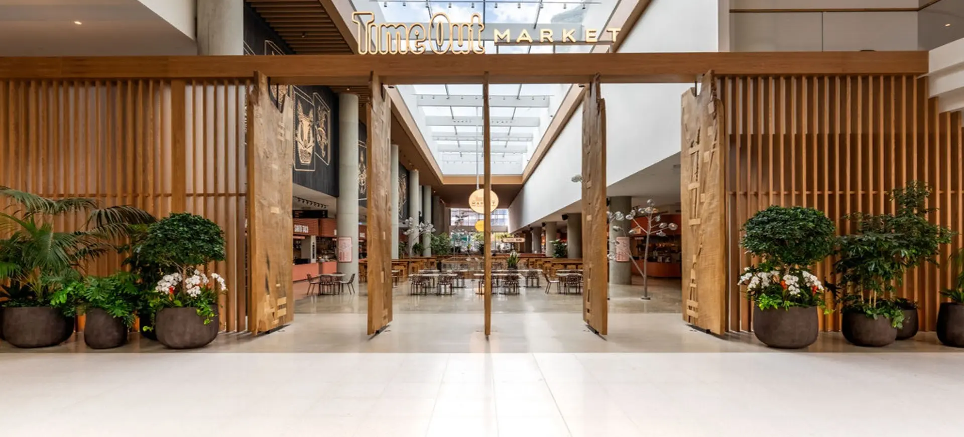 Entrance to Time Out Market with wooden slats, large planters with green plants, and seating area inside under skylight.