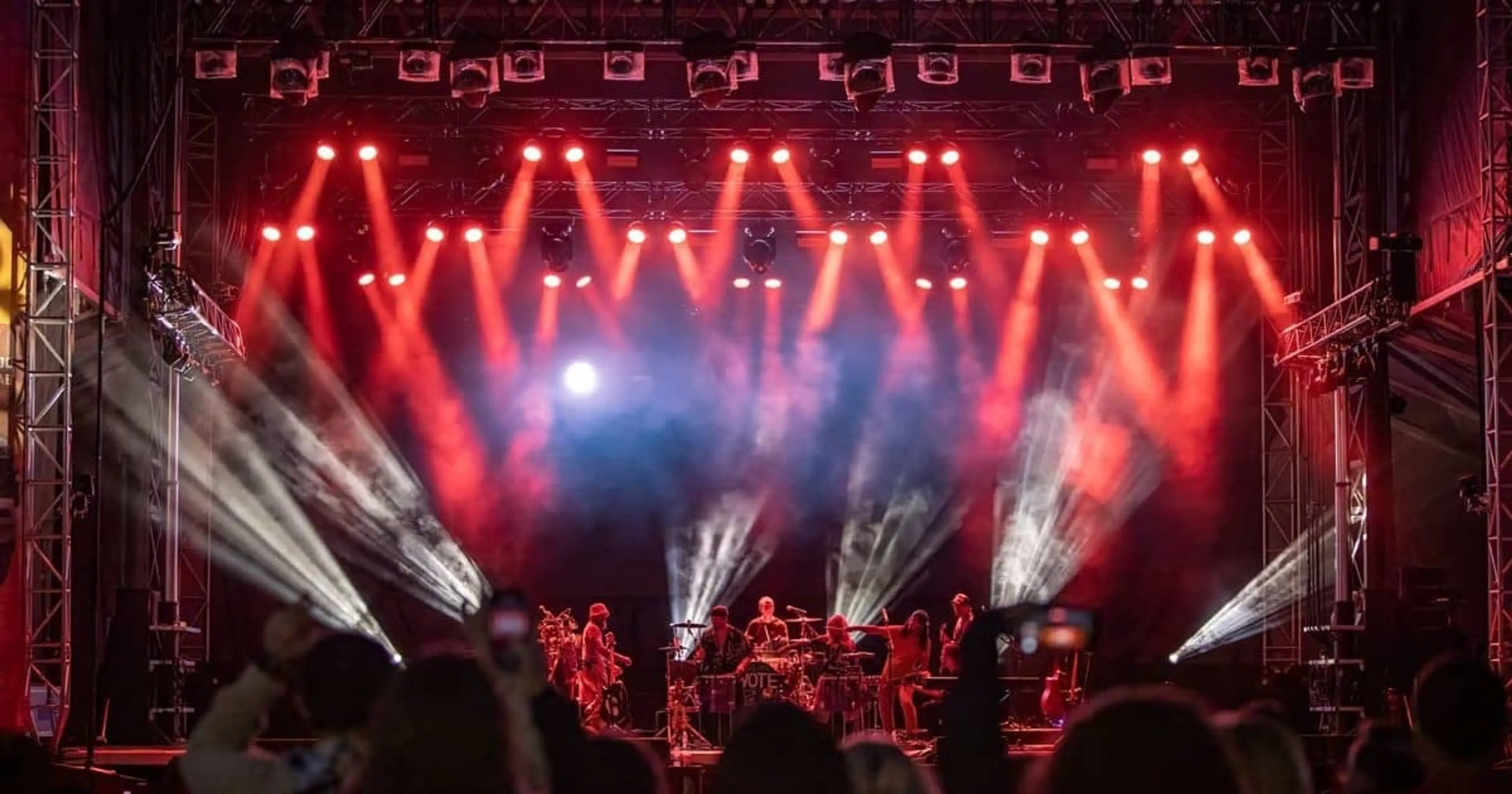 A rock band is playing on a small stage with fog machine and red lights 