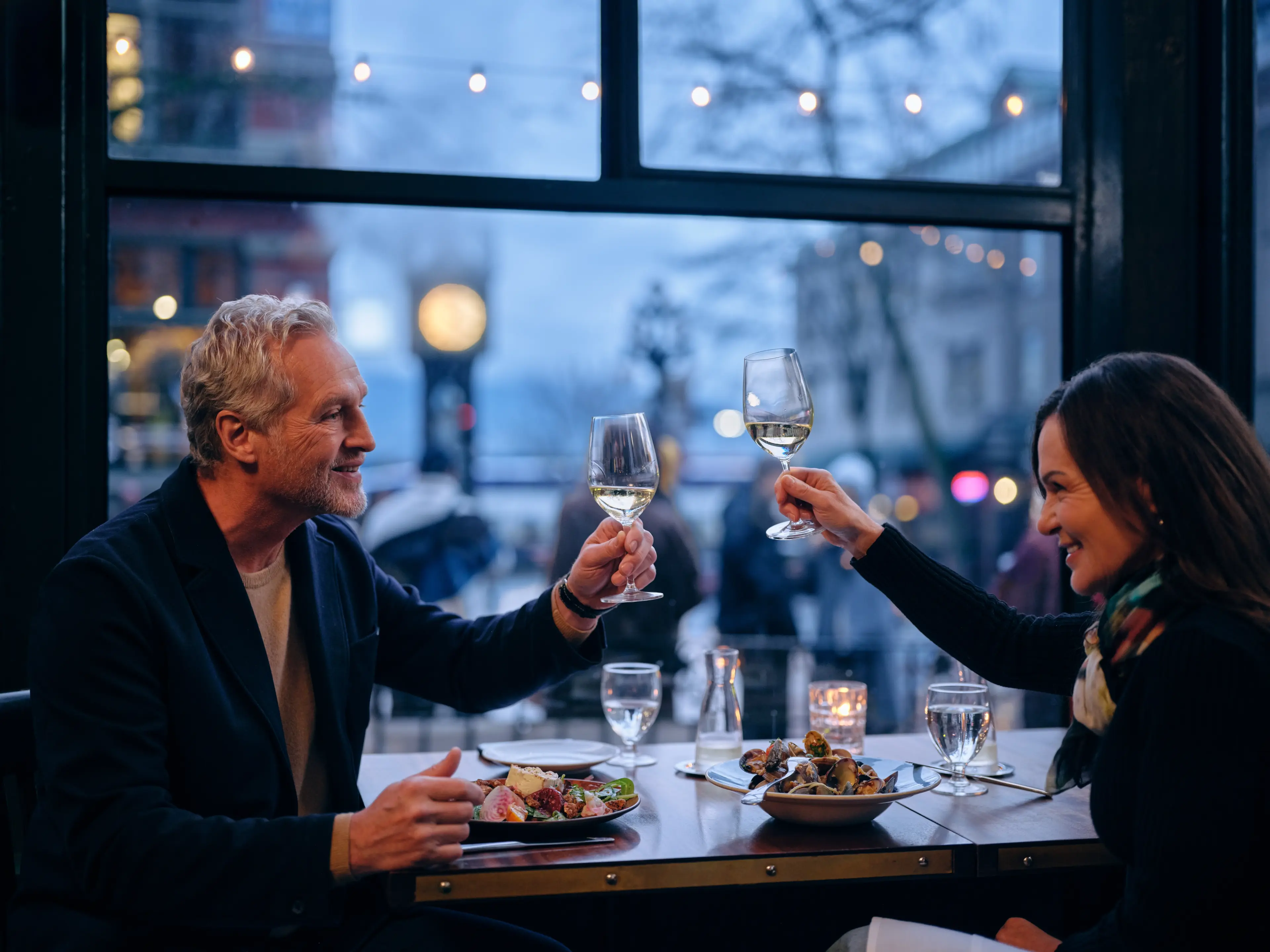 Two people holding up wine glasses at a restaurant in Gastown with the Steam Clock outside the window.