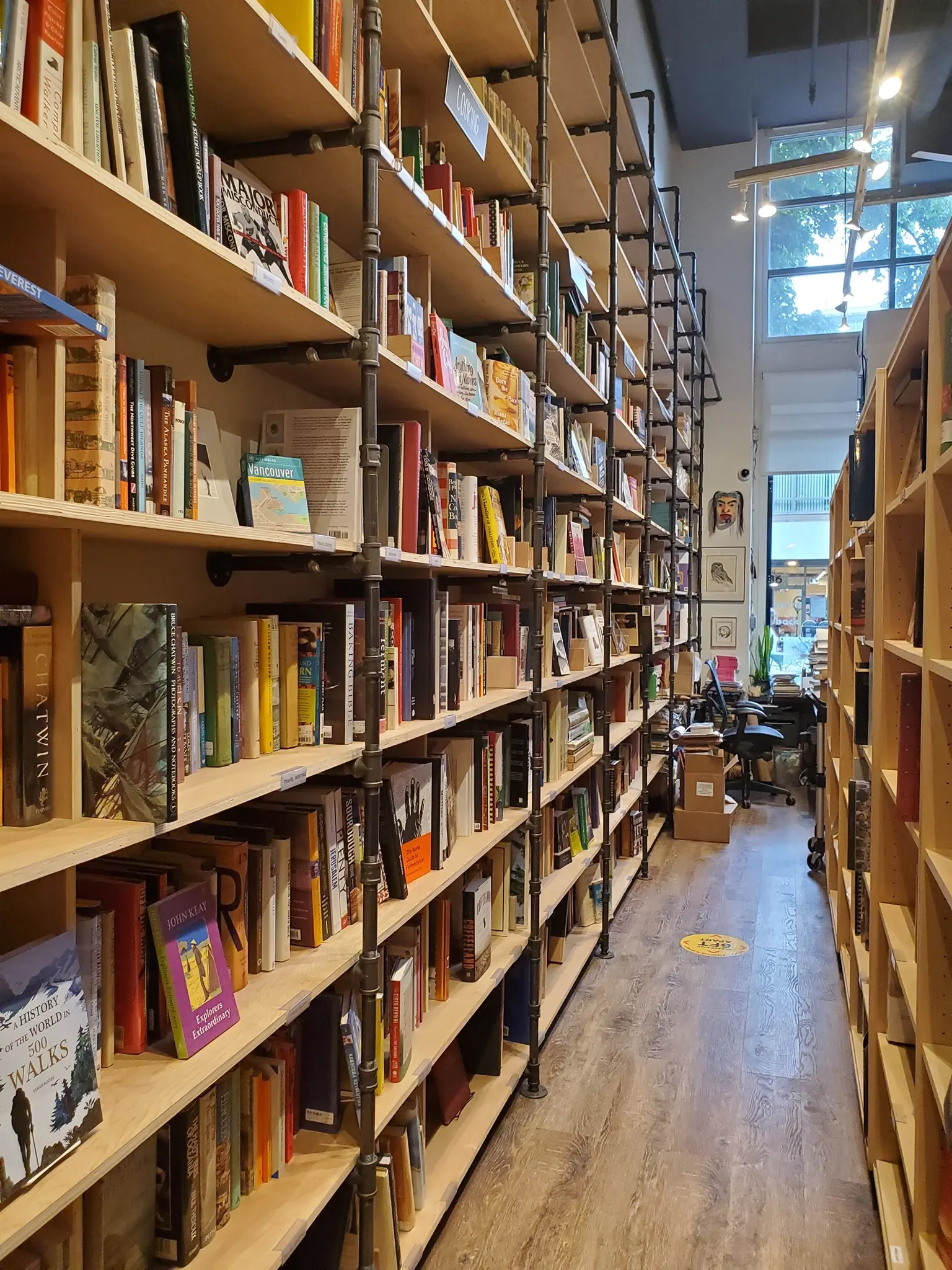 The interor of Massy Books in Vancouver. Tall pipe and wood shelves stretch toward a high ceiling.