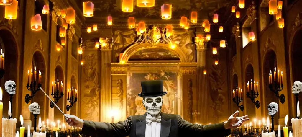 Person in a tuxedo and top hat with skull face paint conducting in a candlelit hall with floating lanterns and skull decorations.