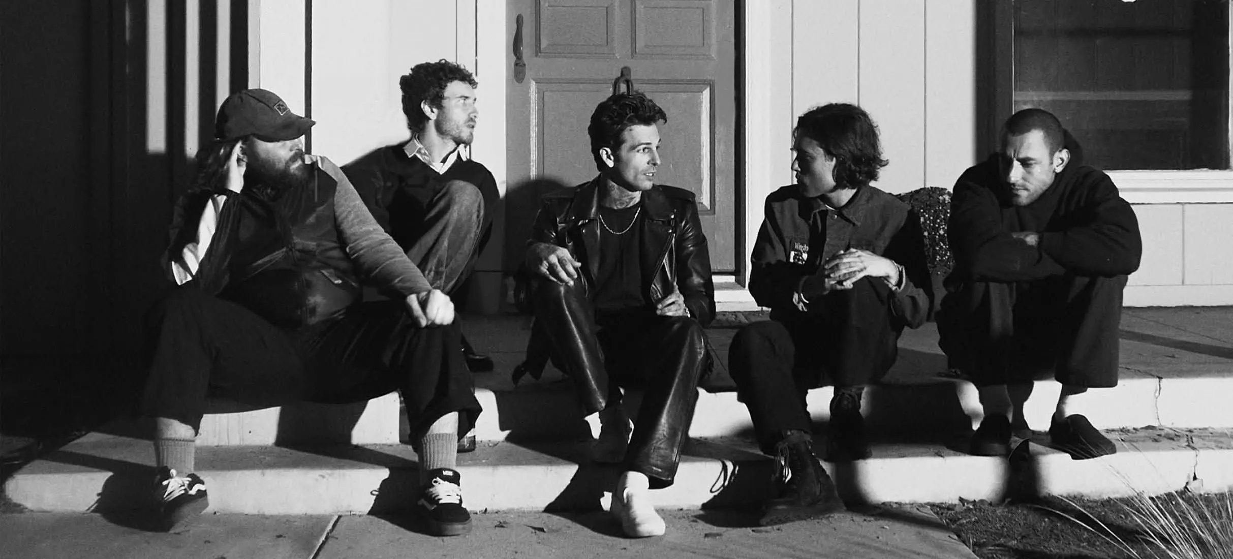Five people sitting on outdoor steps in front of a door, engaged in conversation, in black and white.