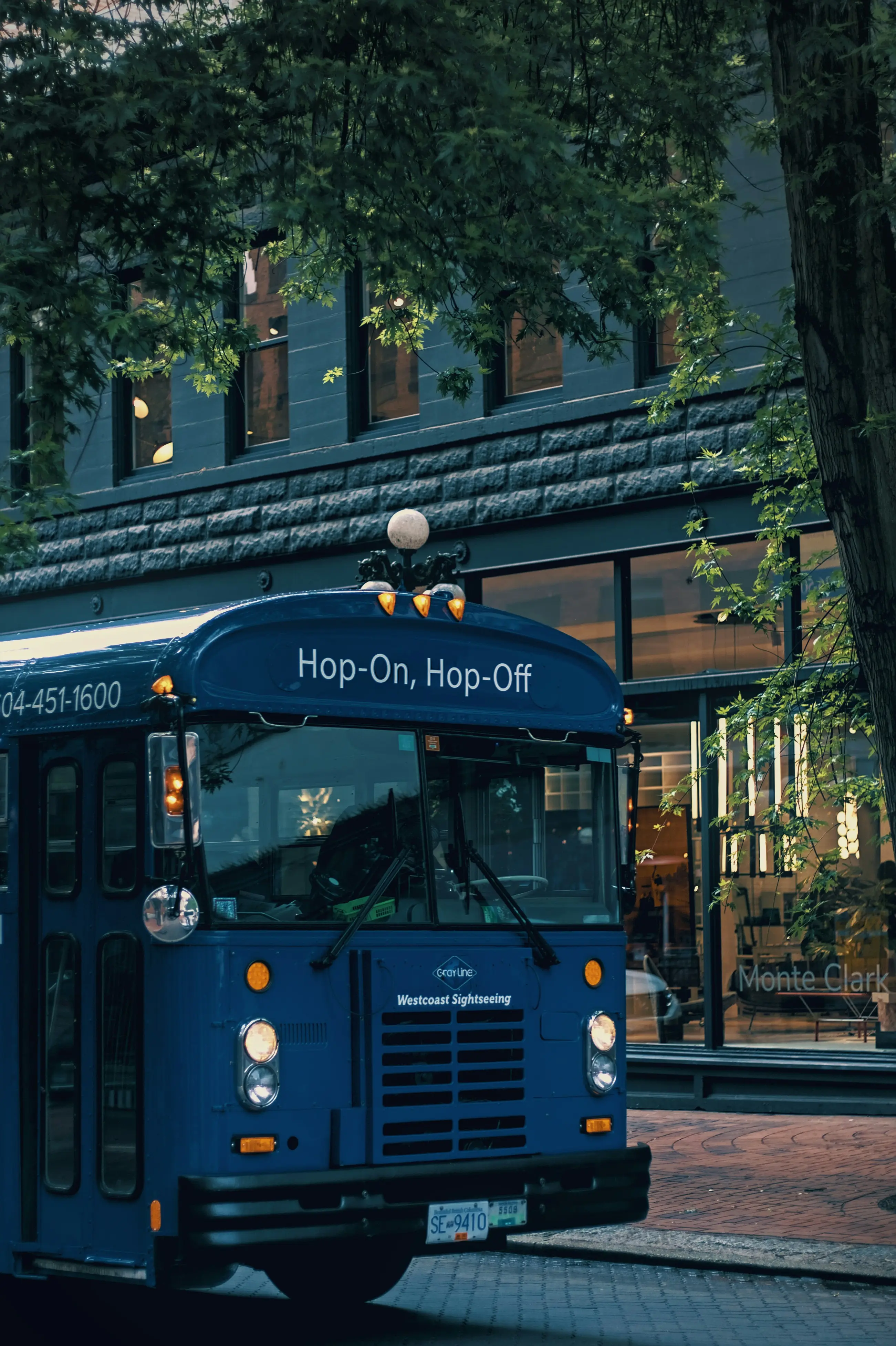 Blue hop-on hop-off sightseeing bus parked on a street in Gastown with trees and a building in the background.