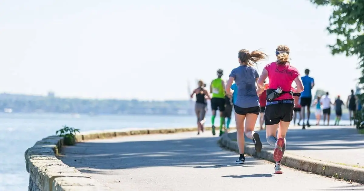 A group of runners in shorts runs along the Vancouver seawall next to the ocean
