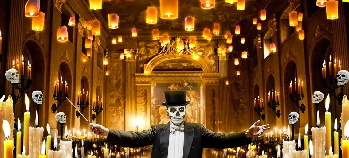Person in skeleton face paint and top hat conducting in a grand hall with floating lanterns, candles, and skull decorations.