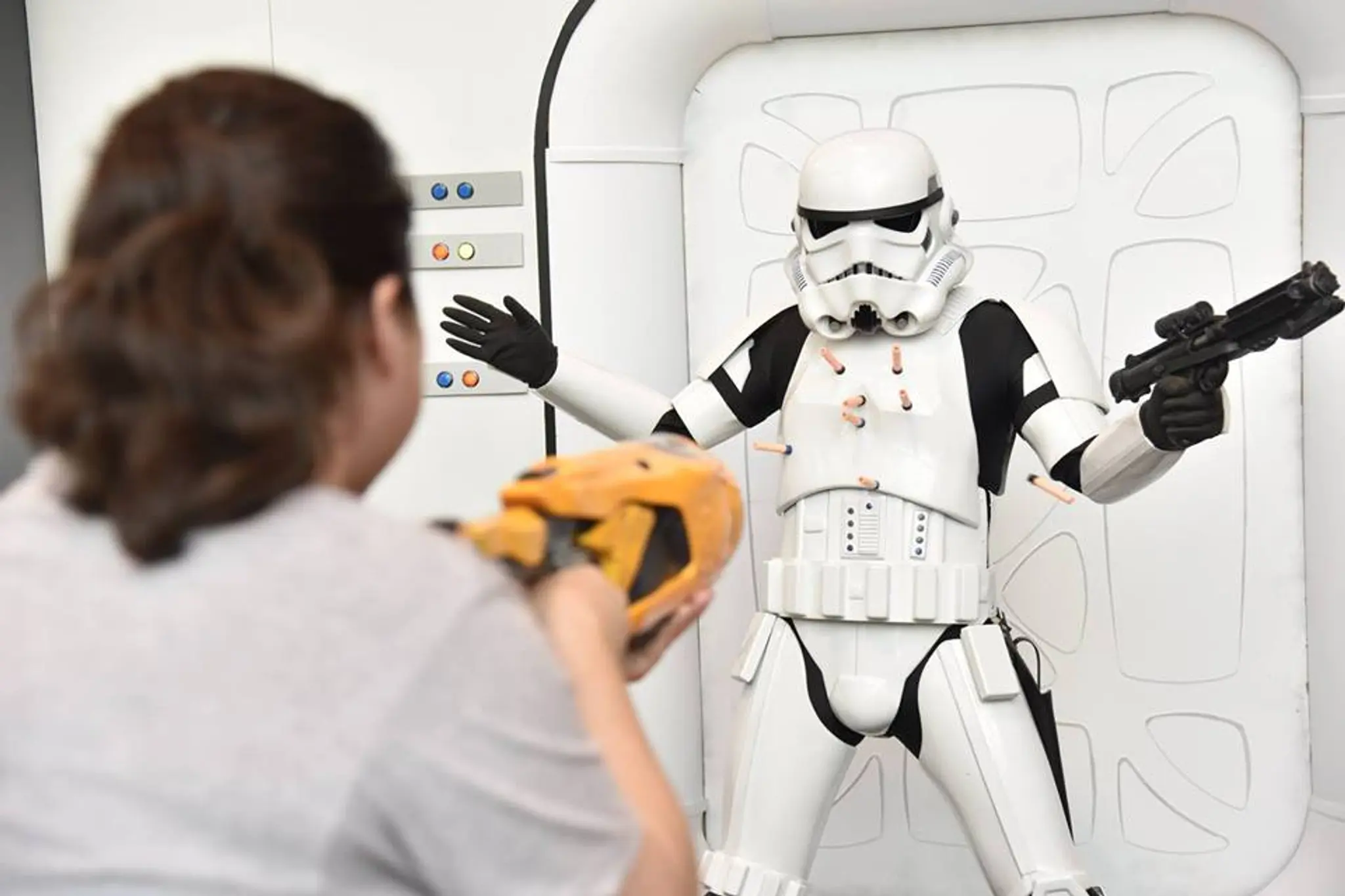 Person aiming a toy gun at a stormtrooper costume with foam darts stuck in the armor at the Vancouver Fan Expo.