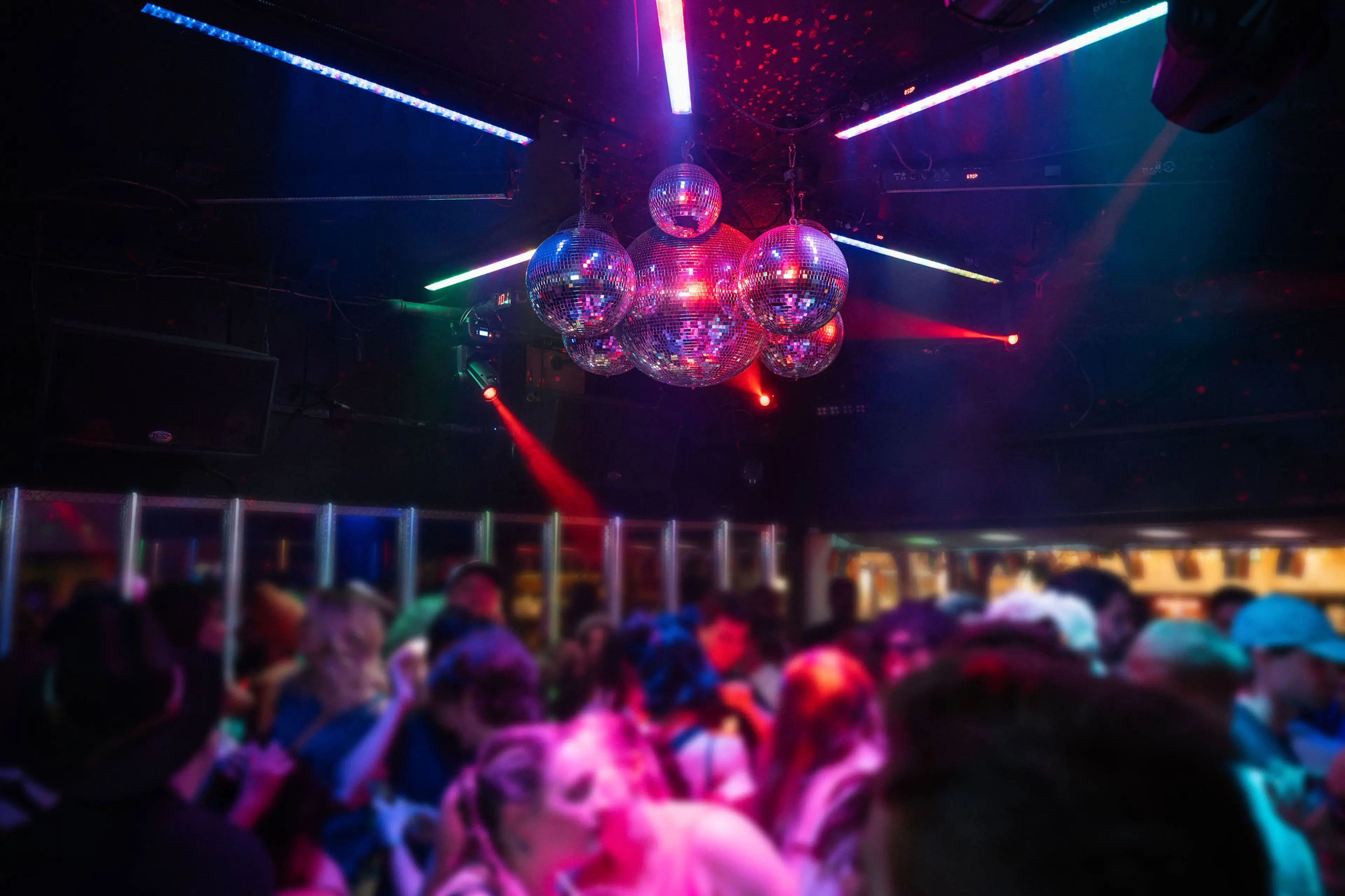 Crowded nightclub with colorful lights and multiple disco balls hanging from the ceiling.