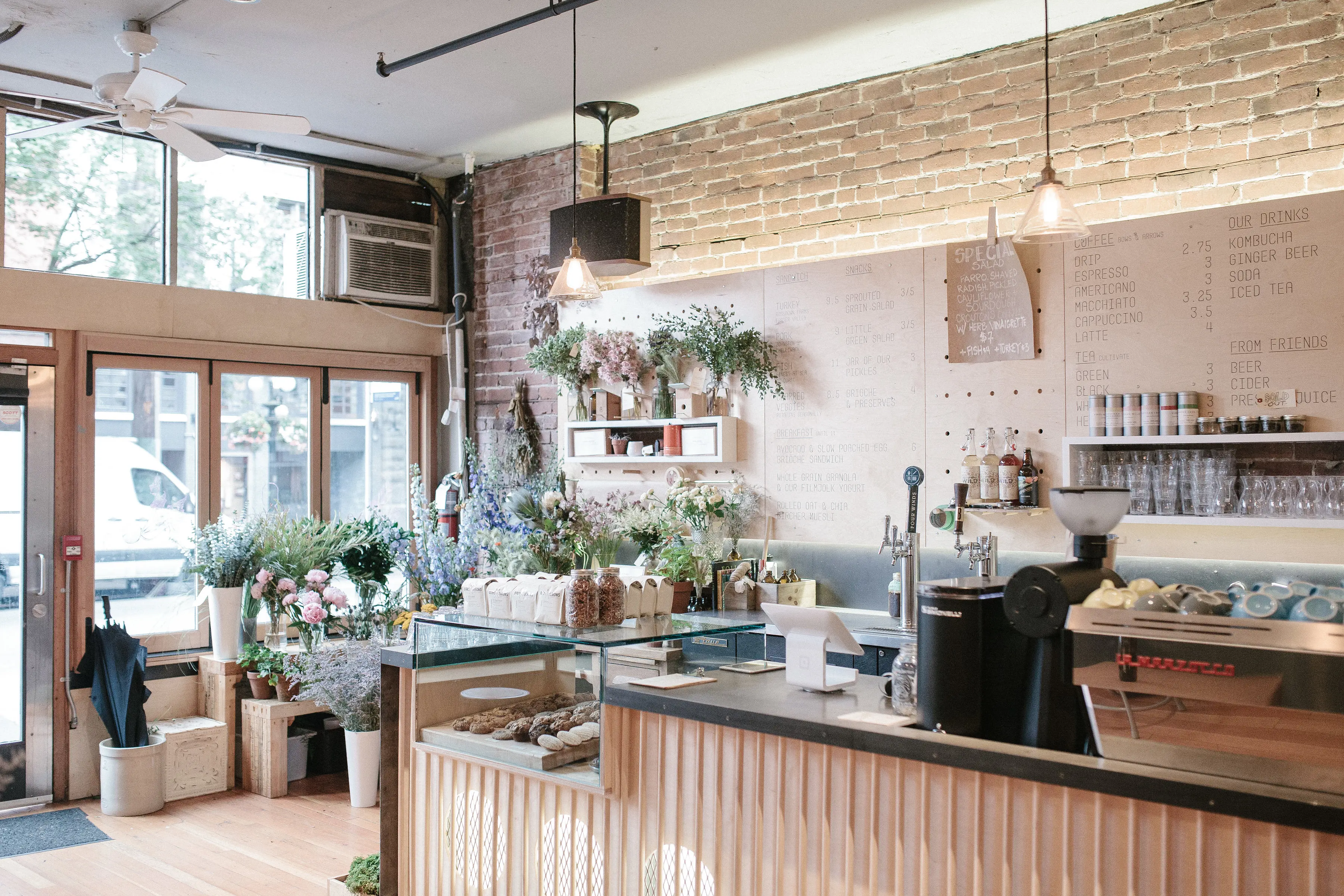 The interior of The Birds and the Beets Cafe in Gastown. There is a handwritten men on the walls, a long counter, and lots of plants and flower arrangements.