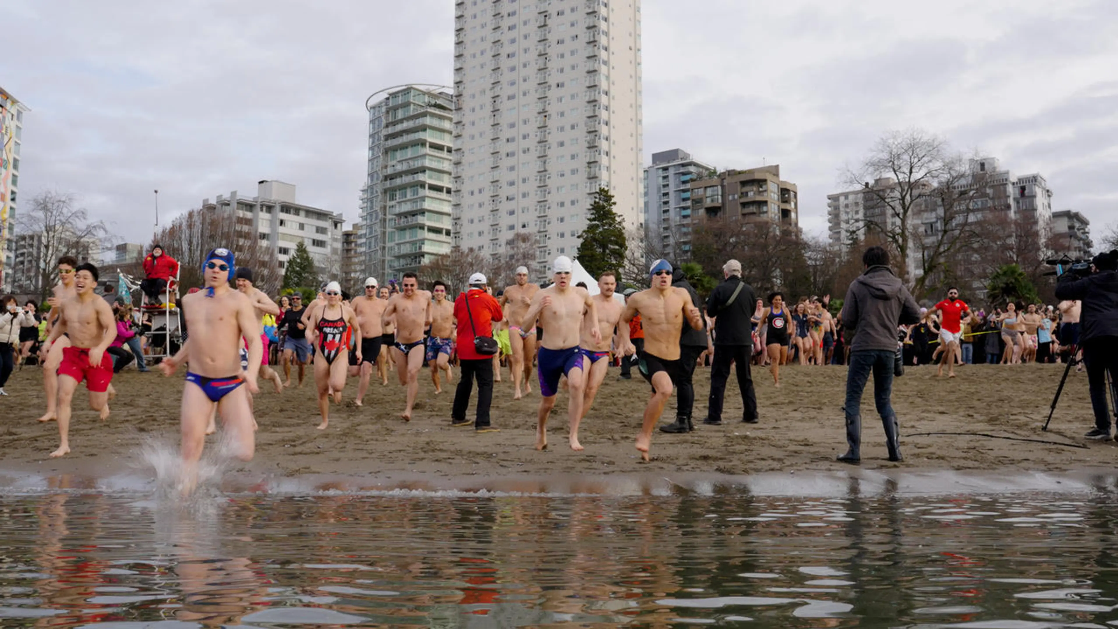 Men in Speedos run towards the camera in the water at the start of the Vancouver Polar Bear Swim