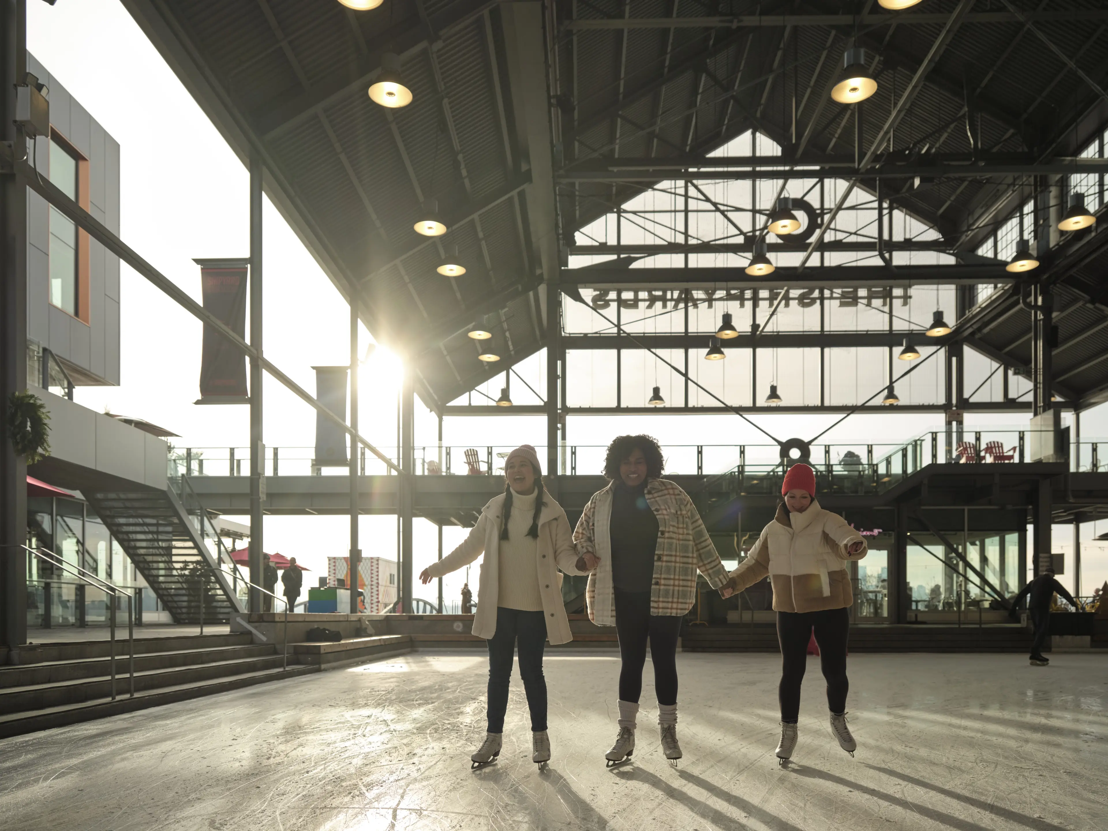 Three friends hold hands as they skate at the Shipyards Skate Plaza in North Vancouver.