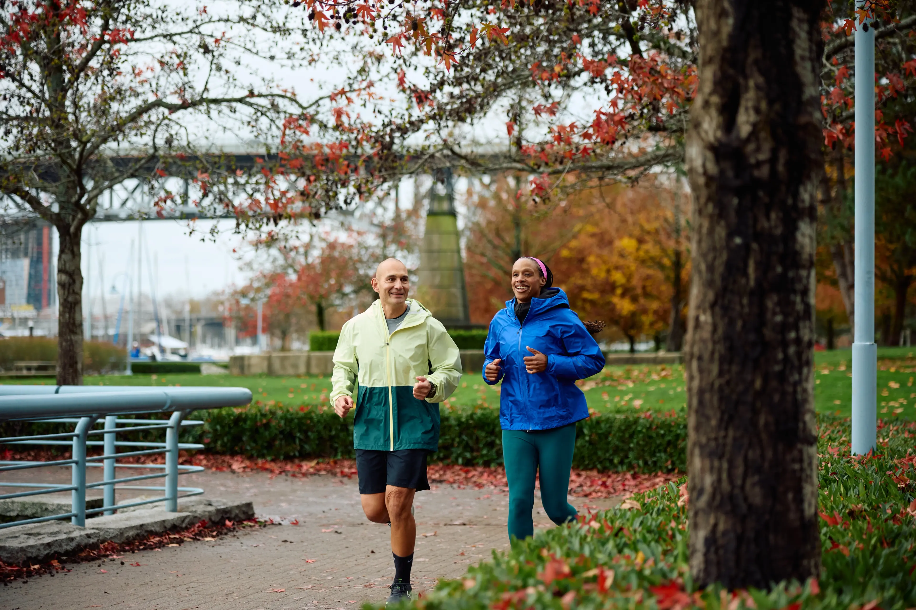 Two people running along the water in the fall in David Lam Park in Vancouver.