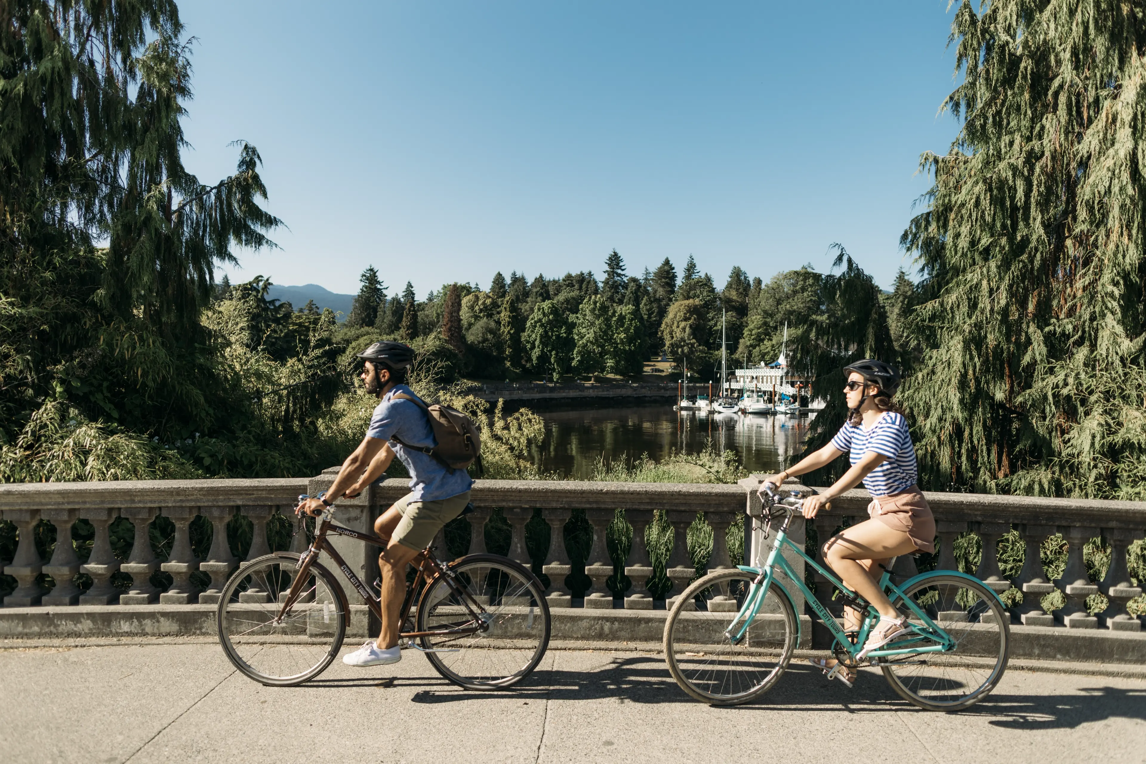 Two people ride on the Stanley Park Seawll near the rowing club. 