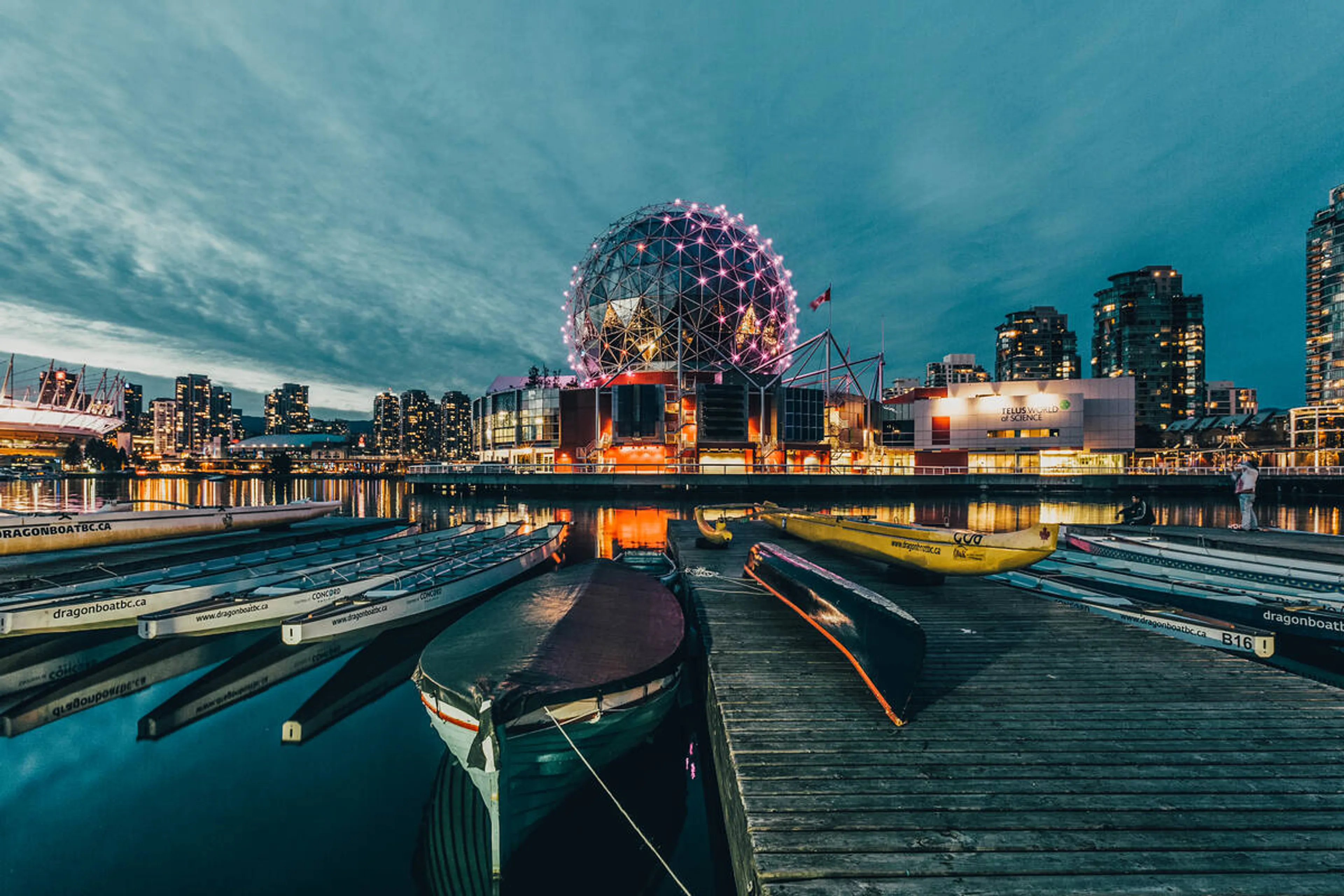 Science World in Vancouver lit up at night with docked boats in the foreground