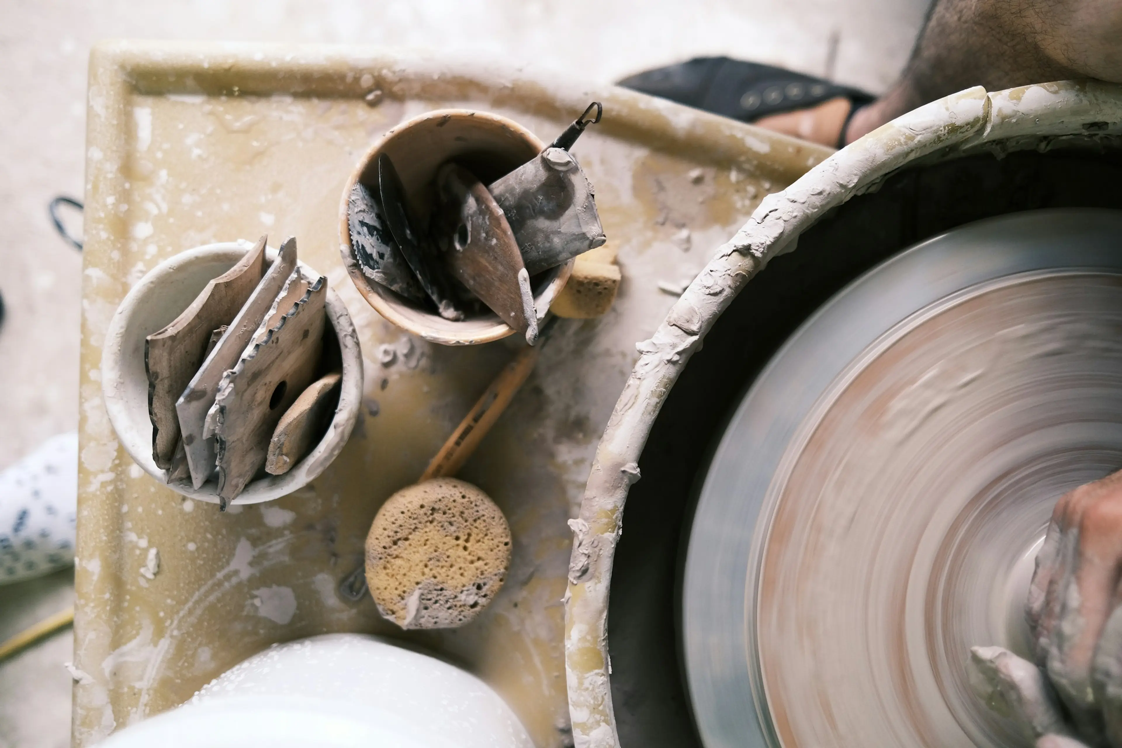 Overhead shot of hands on a pottery wheel with clay shaping tools nearby.