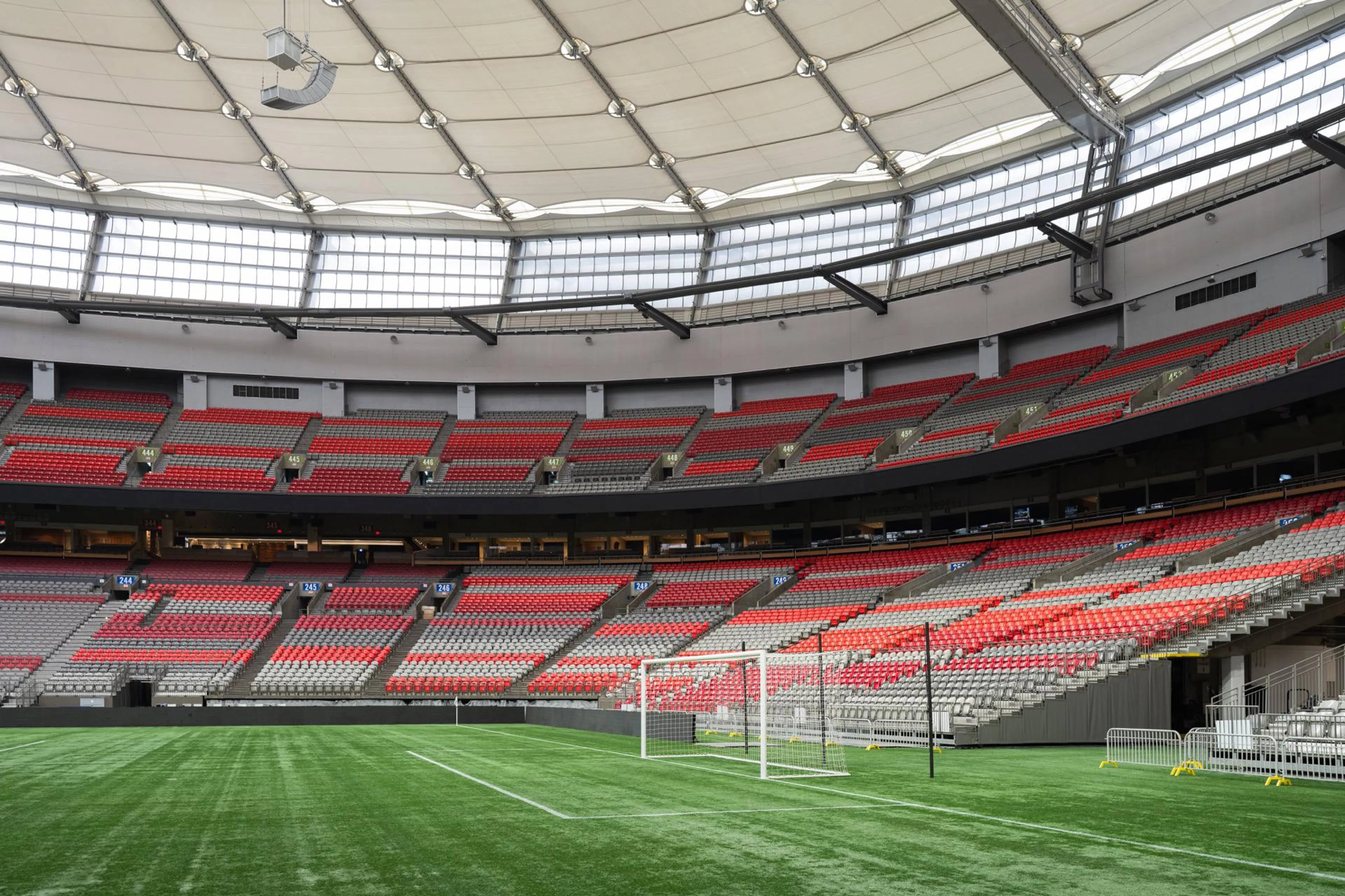 Empty indoor soccer stadium with red and gray seats and a white goalpost on green artificial turf.