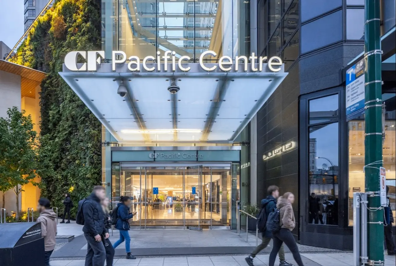 Entrance to CF Pacific Centre with glass doors and people walking on the sidewalk in front.