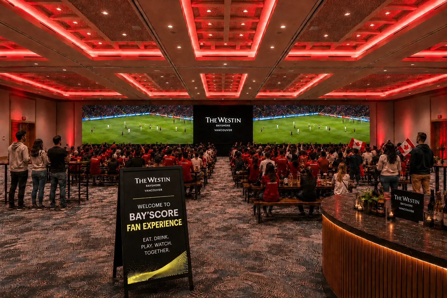 Large group of people watching a soccer match on two big screens in a room with red ceiling lights, some holding Canadian flags.