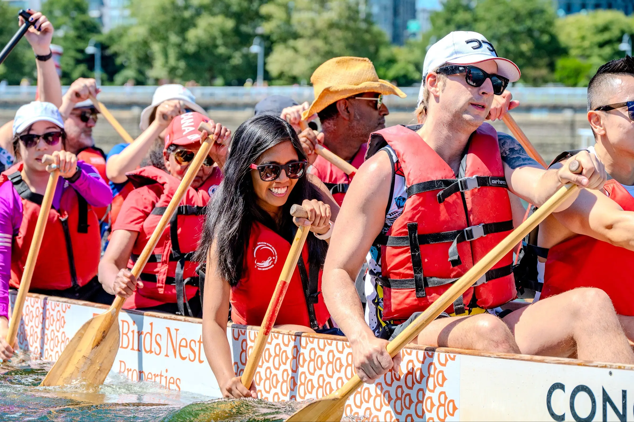 A group of people wearing red life jackets paddling a dragon boat on water during a sunny day.
