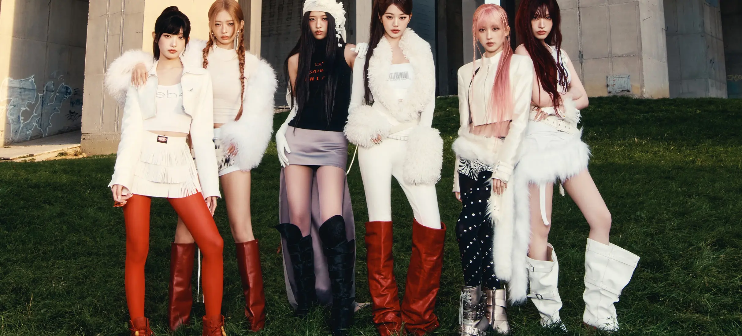 Six people standing on grass in front of a concrete structure, wearing stylish white and red outfits with boots.