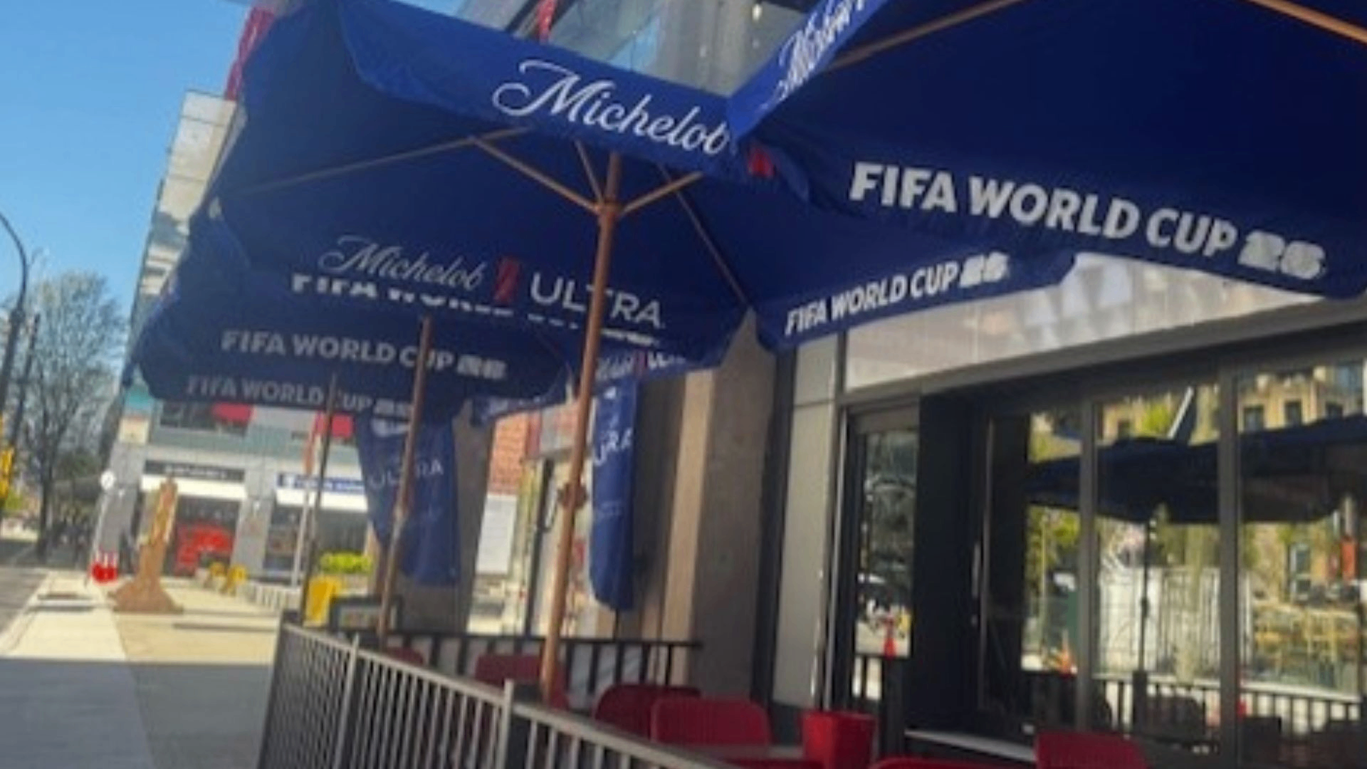 Outdoor seating area with blue umbrellas displaying Michelob Ultra and FIFA World Cup 2026 logos on a sunny day.