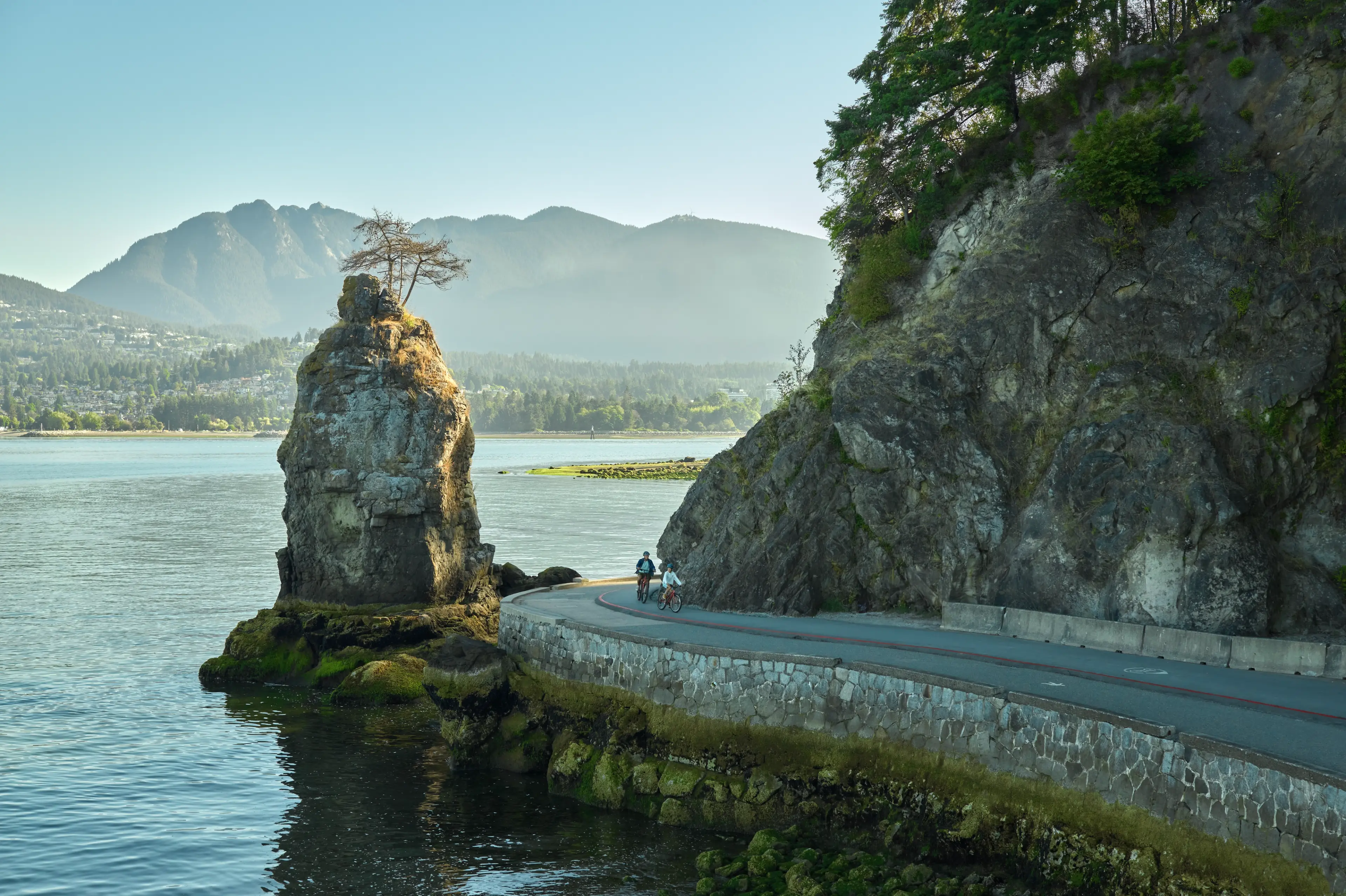 The Siwash Rock along the Vancouver seawall with ocean and mountains in the background.