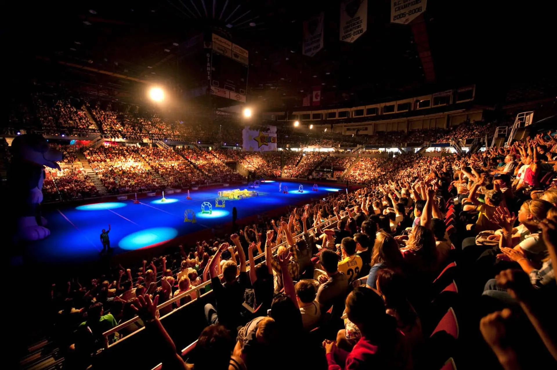 A crowd of cheering fans at an indoor stadium with blue spotlights shining.