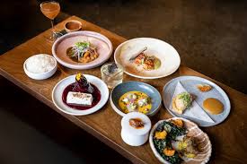 Wooden table with various plated gourmet dishes and a cocktail glass, including rice, seafood, and desserts.