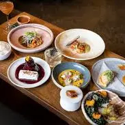 Wooden table with various plated gourmet dishes and a cocktail glass, including rice, seafood, and desserts.