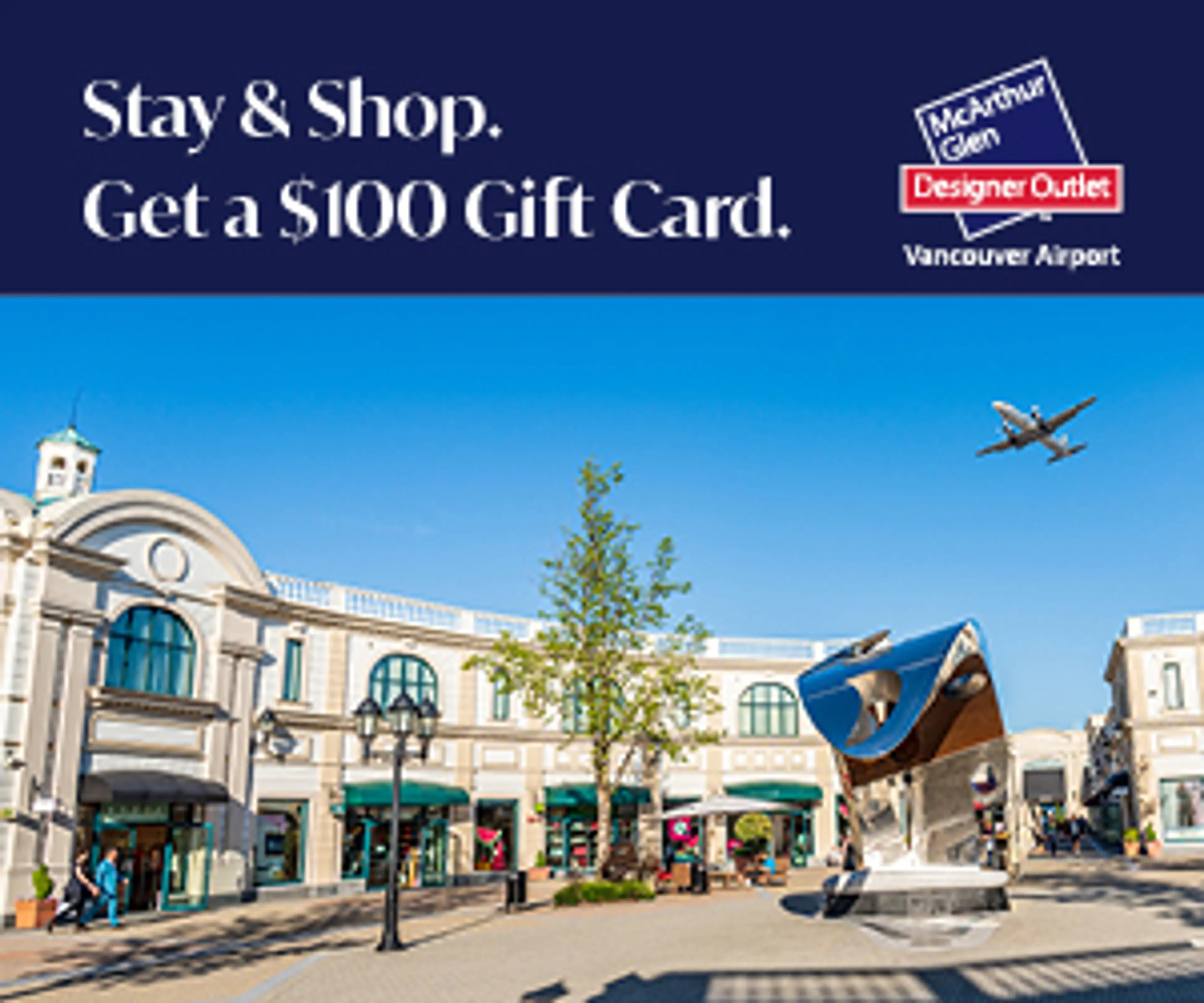 McArthur Glen Designer Outlet Vancouver Airport with shops, a tree, a modern sculpture, and an airplane flying overhead under a clear blue sky.