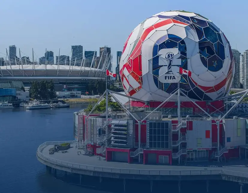 Large spherical building painted like a soccer ball with FIFA logo near waterfront and stadium in background